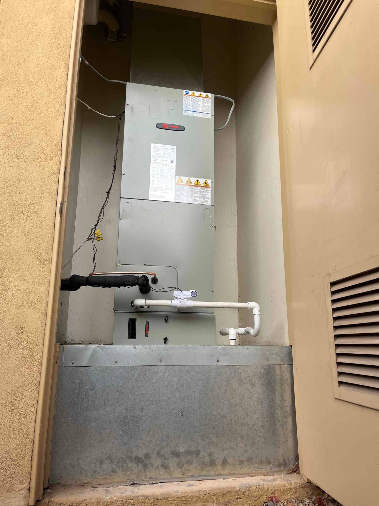 New air handler installed in exterior closet with insulated refrigerant line, condensate trap and cleanout, and sealed return plenum.