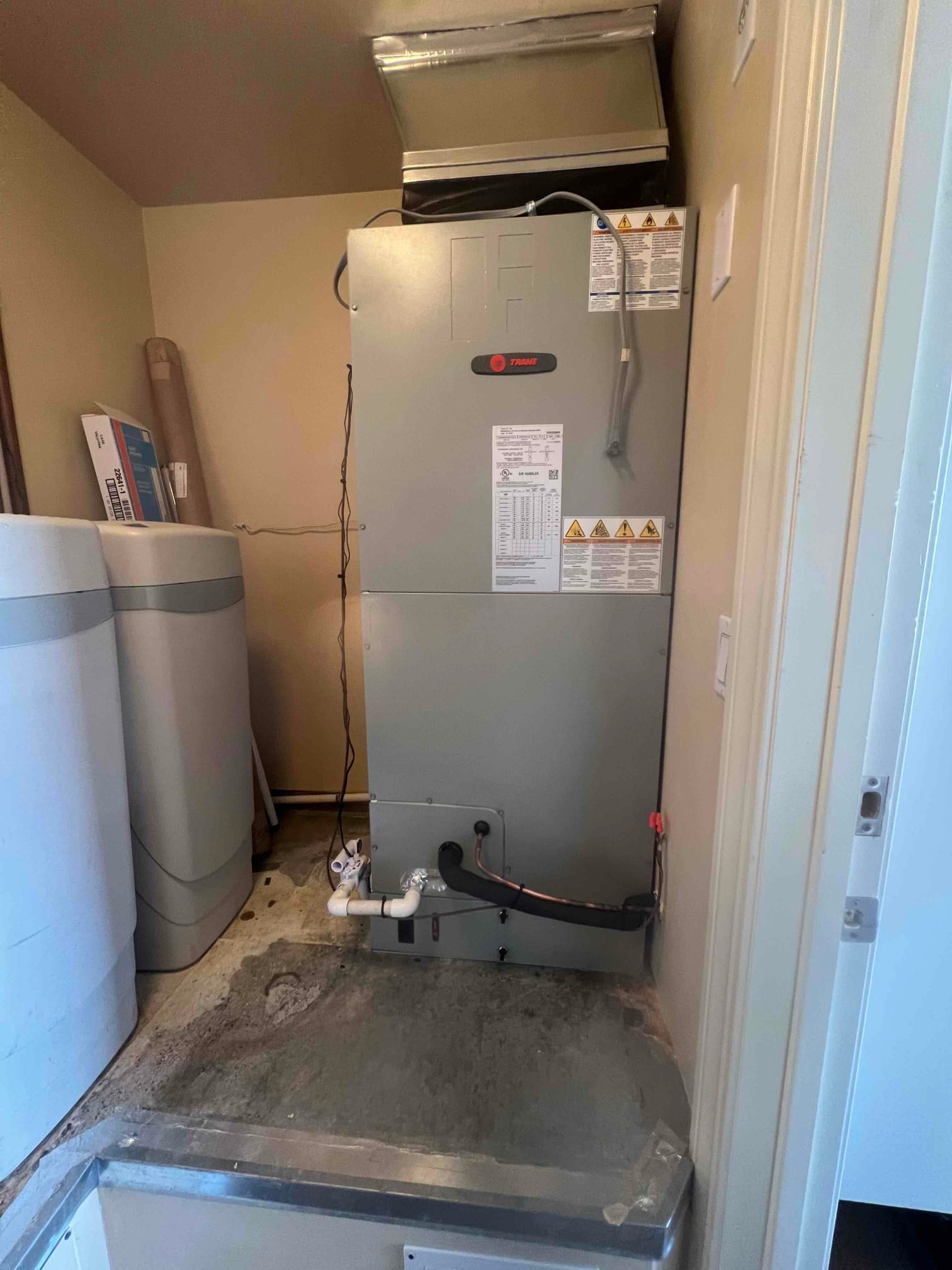 New air handler installed on a platform with insulated refrigerant line, PVC condensate drain, and connected supply plenum above.