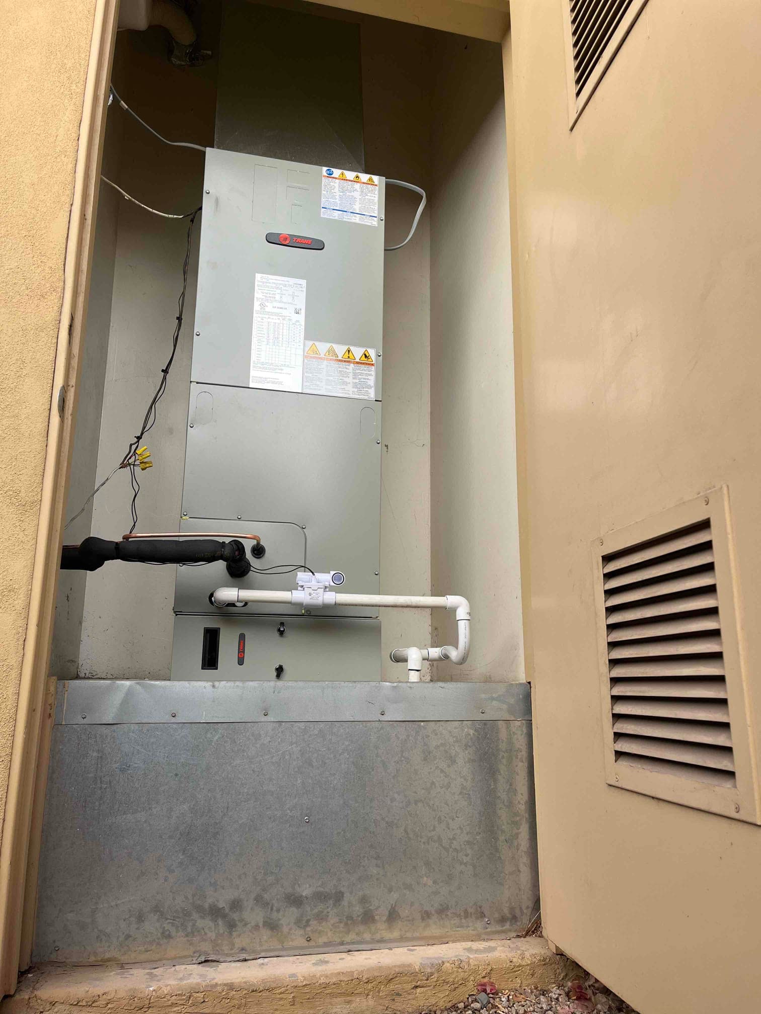 New air handler installed in a utility closet with insulated suction line, condensate trap and safety float switch on the drain.