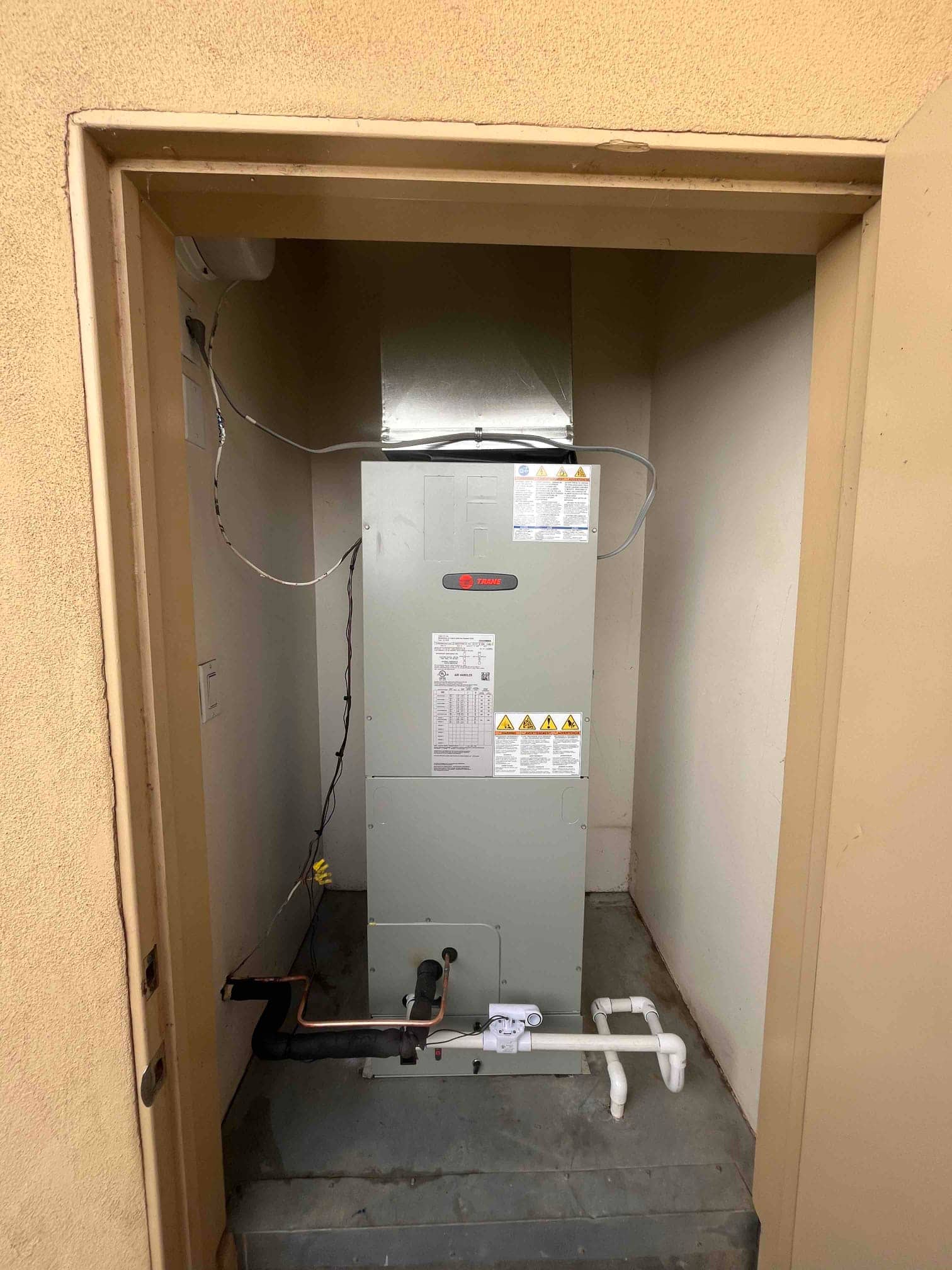 New air handler set in a closet with insulated refrigerant line, condensate drain with cleanout, and connected supply plenum.