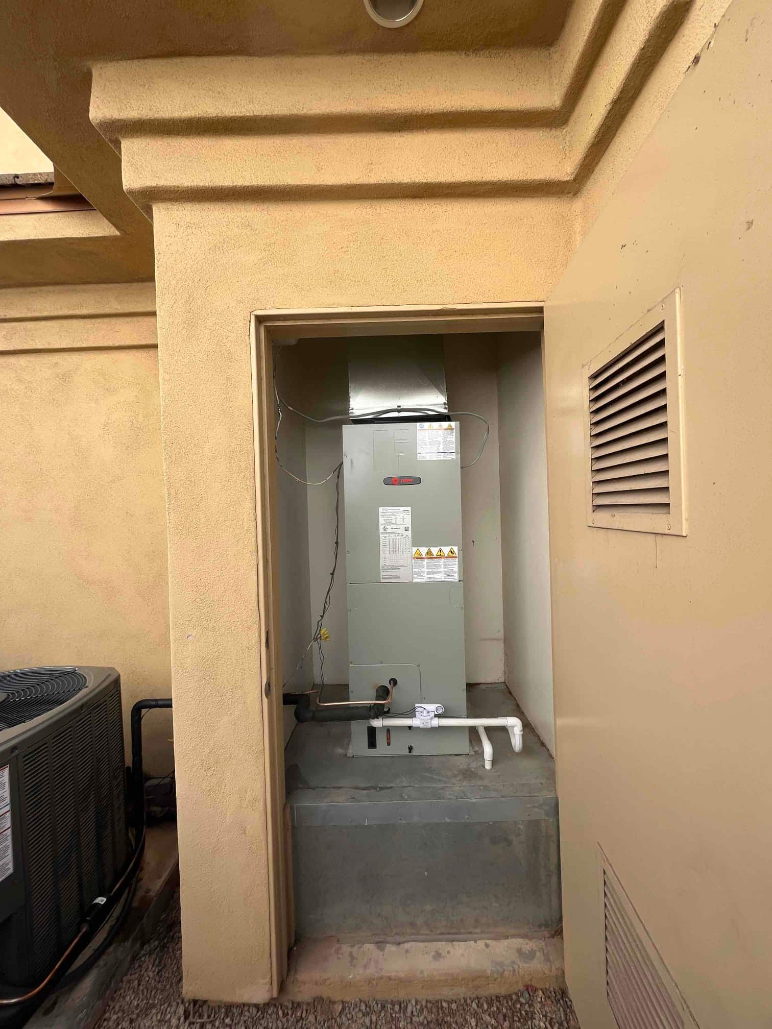 New air handler set in an exterior closet with connected condensate drain and insulated refrigerant lines to the outdoor unit.
