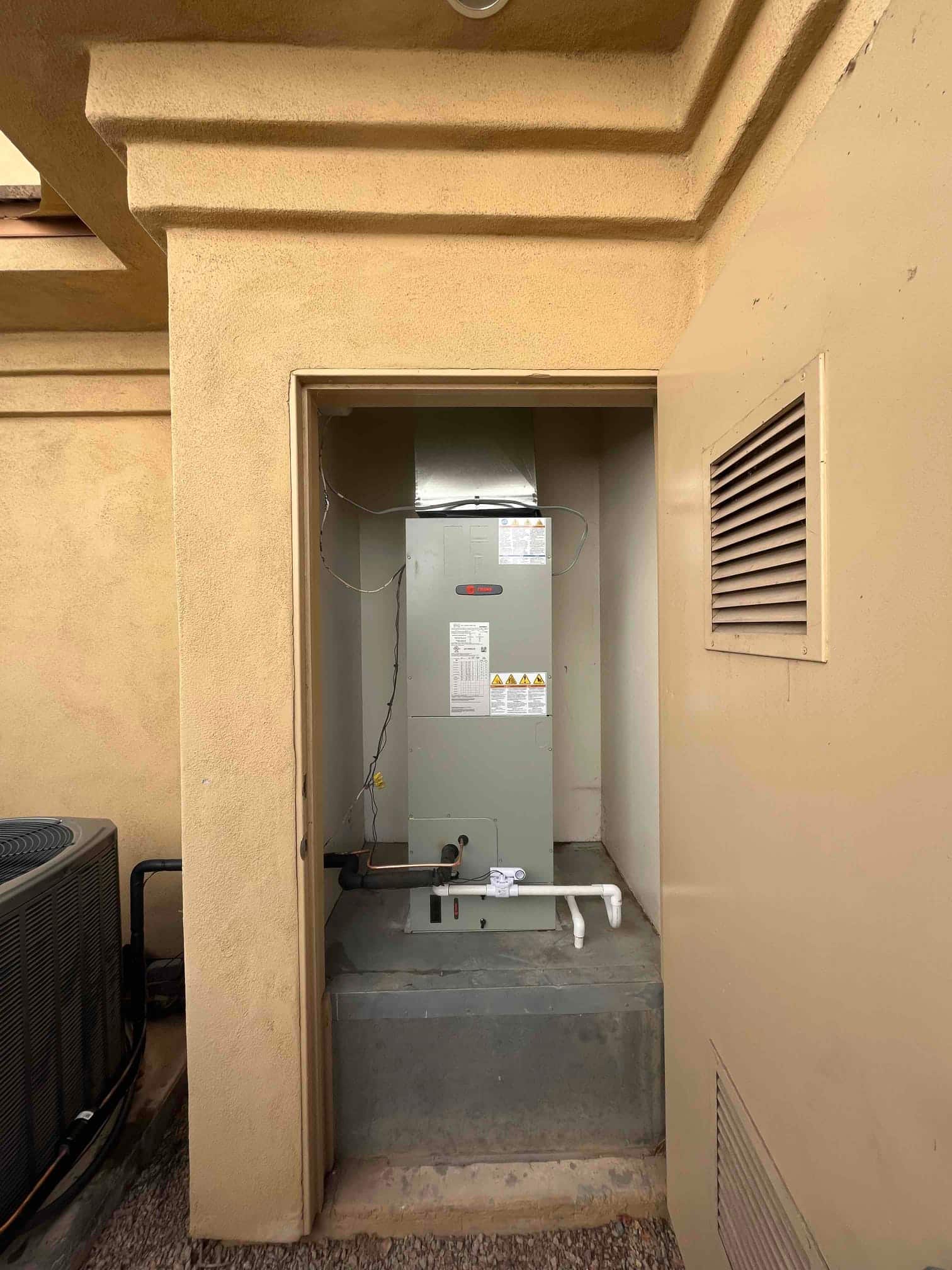 New air handler set on a platform with insulated refrigerant lines and PVC condensate drain, adjacent to the outdoor unit.
