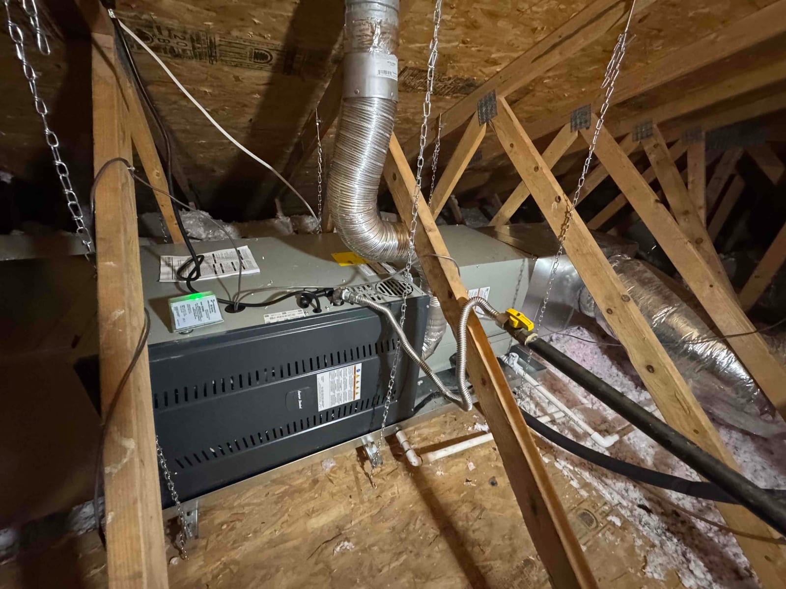 New attic air handler hung with support chains, connected to flexible ductwork, drain piping, and insulated refrigerant lines.