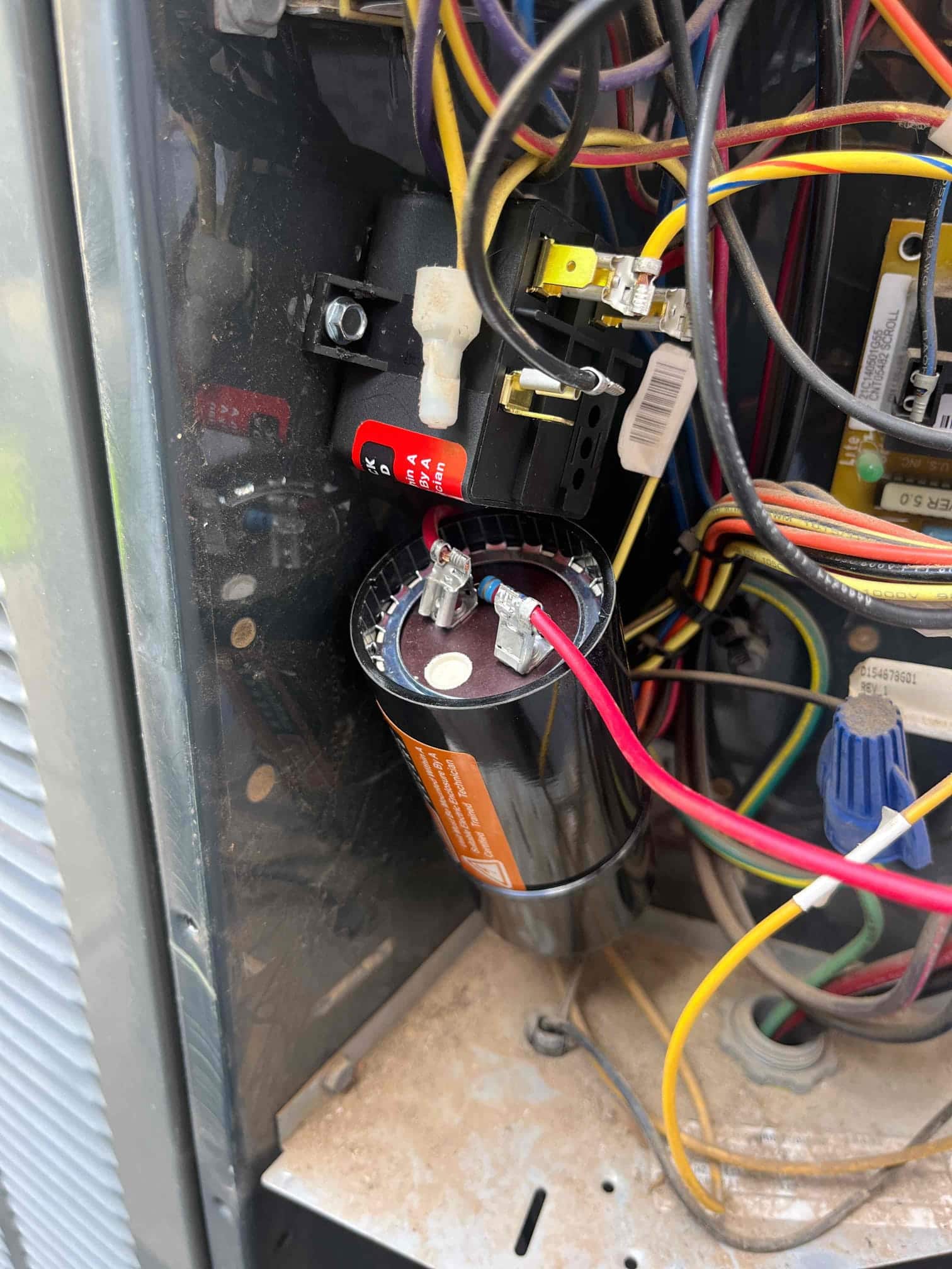 New dual-run capacitor installed inside the condenser control panel with connected red and brown wires and clean terminals.