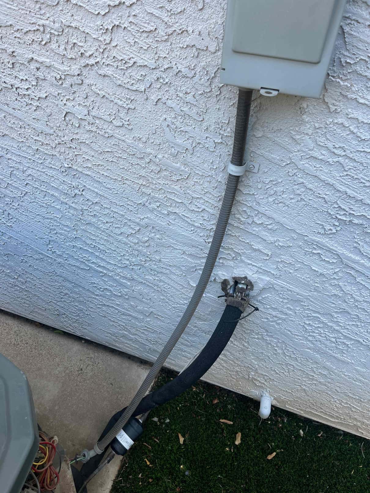 New flexible condenser whip and secured electrical conduit installed at the outdoor unit, with insulated refrigerant line entering the wall.