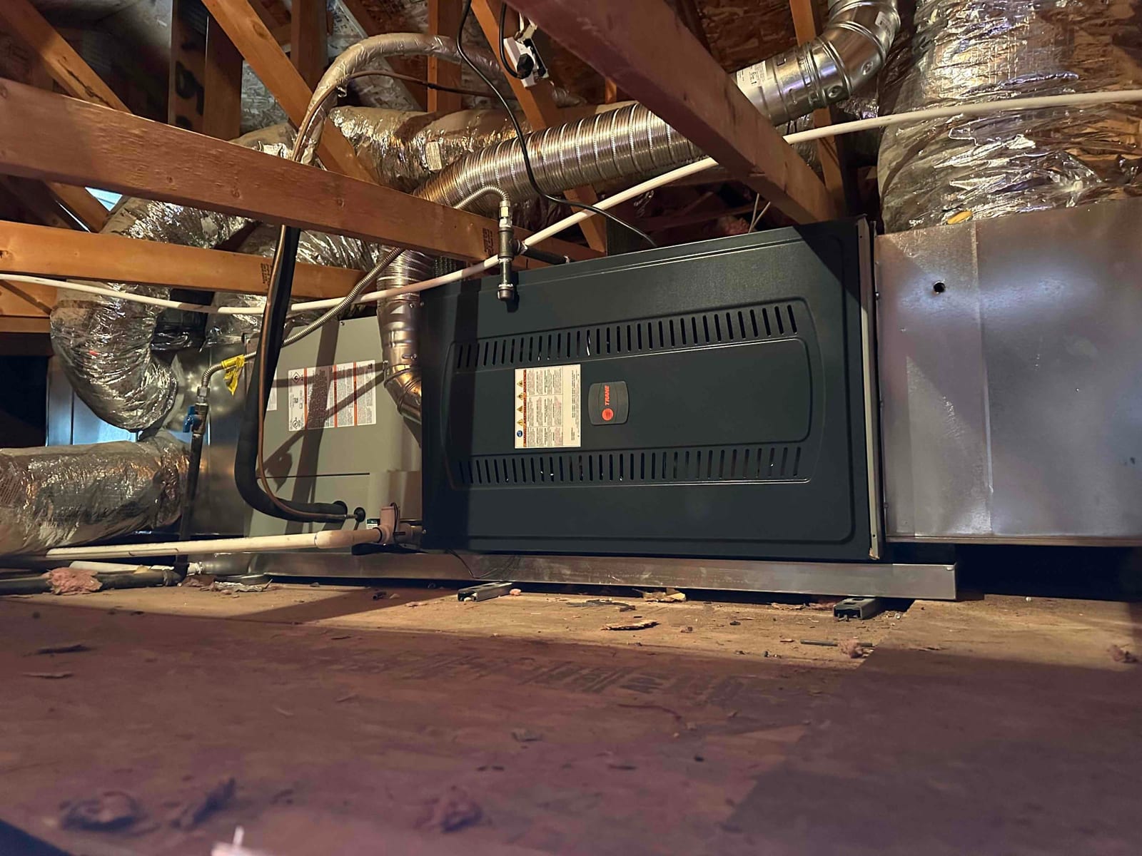 New gas furnace and evaporator coil installed in attic with connected ductwork, refrigerant lines, and condensate drain piping secured.