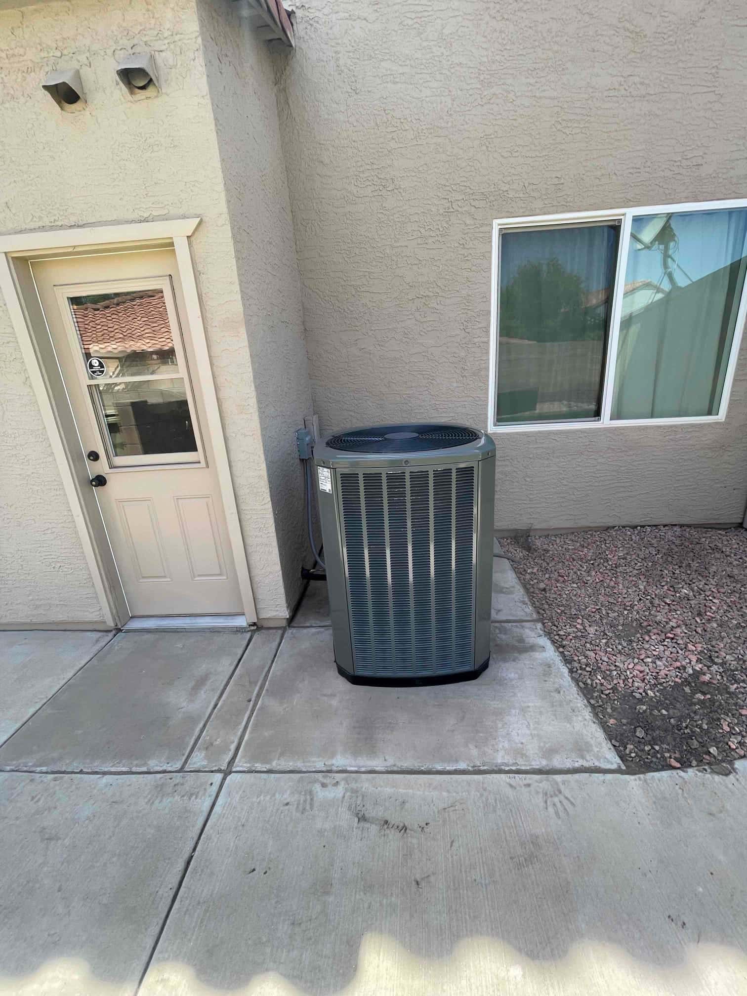 New outdoor heat pump condenser set on a level concrete pad with electrical whip and line set routed to the wall.
