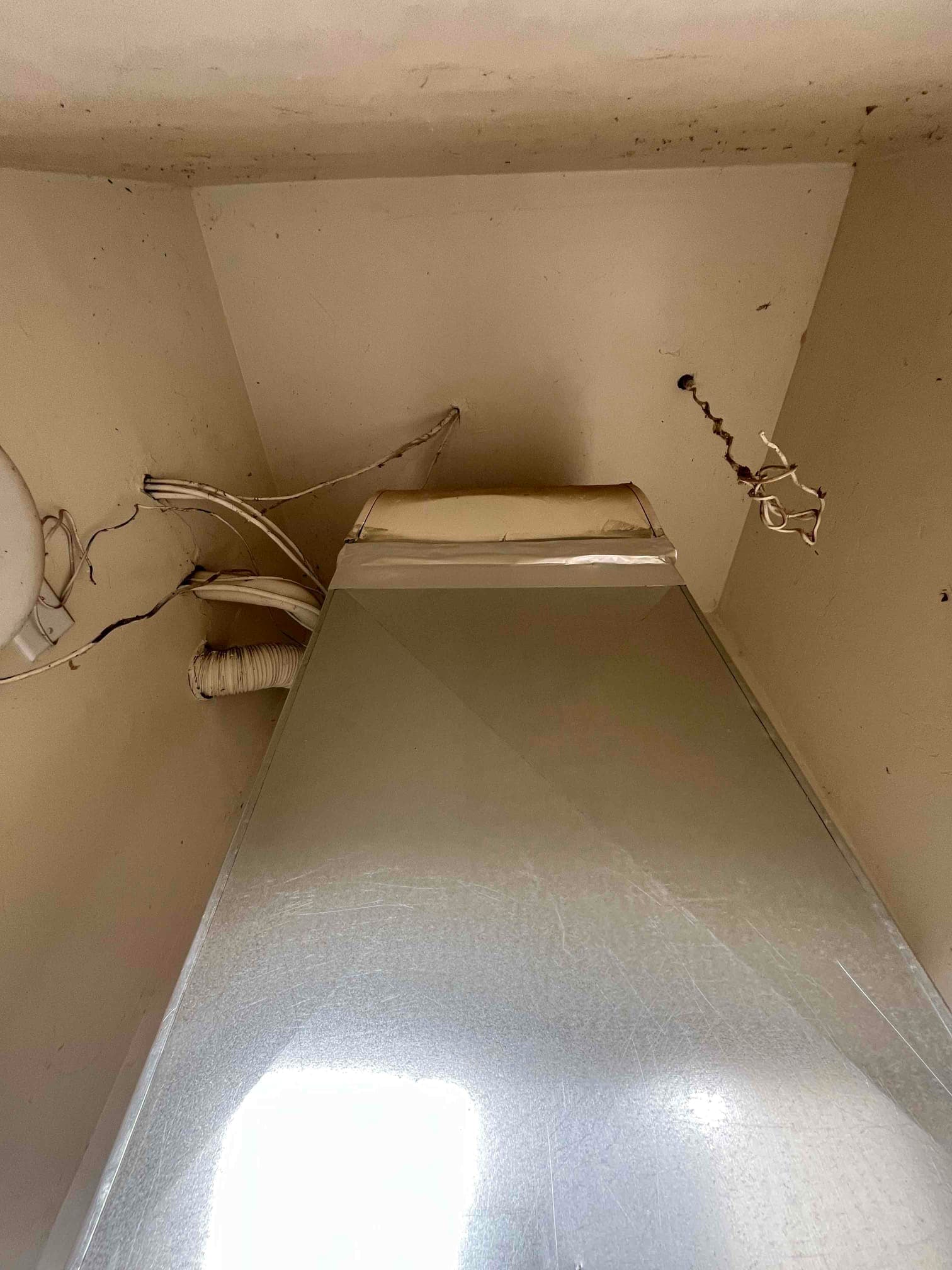 New vertical sheet-metal duct or air handler cabinet installed in a closet space with connected wiring and a flexible drain or vent line.