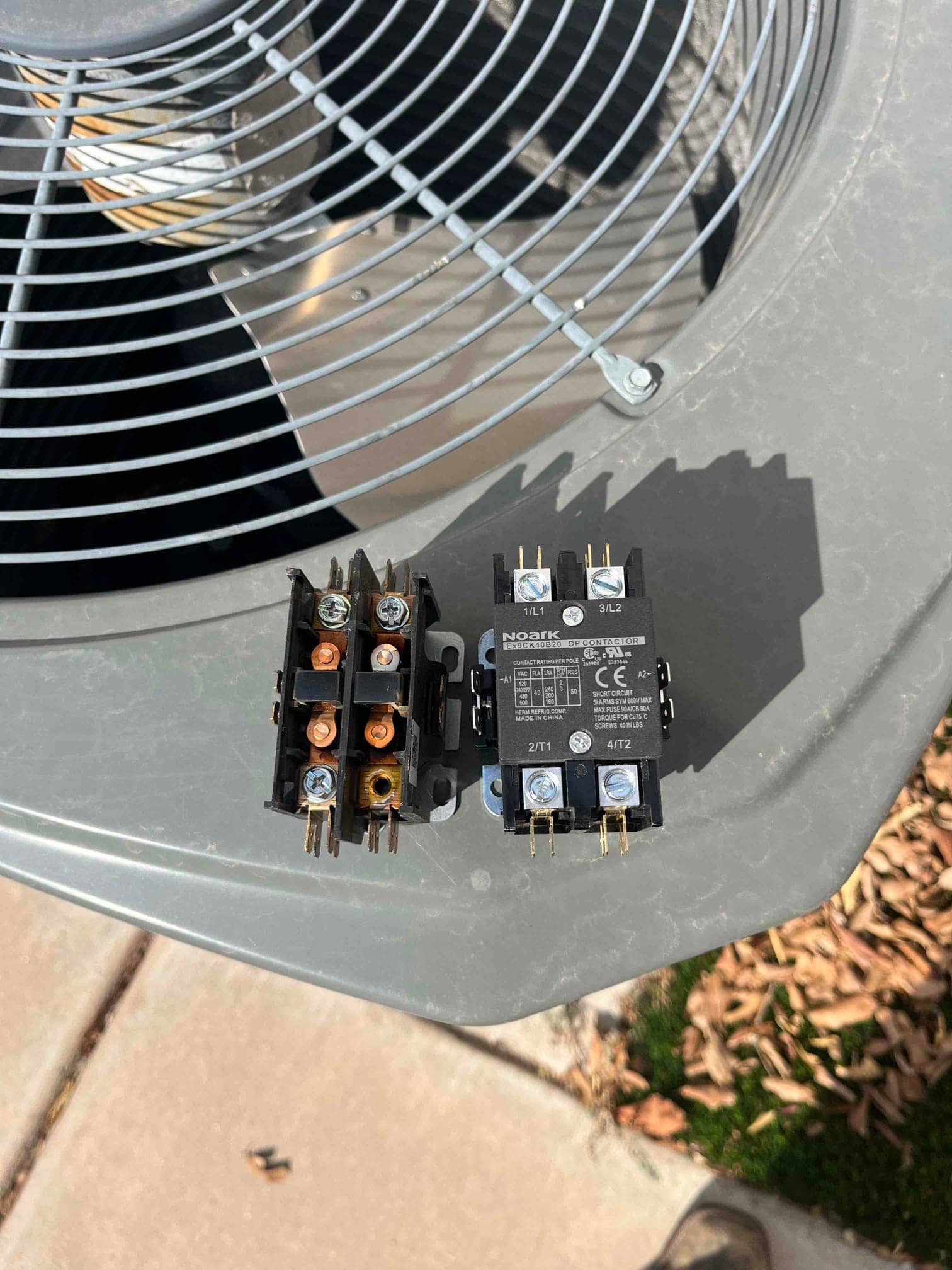 Old contactor with burnt contacts removed next to new replacement contactor on top of the outdoor condenser unit.