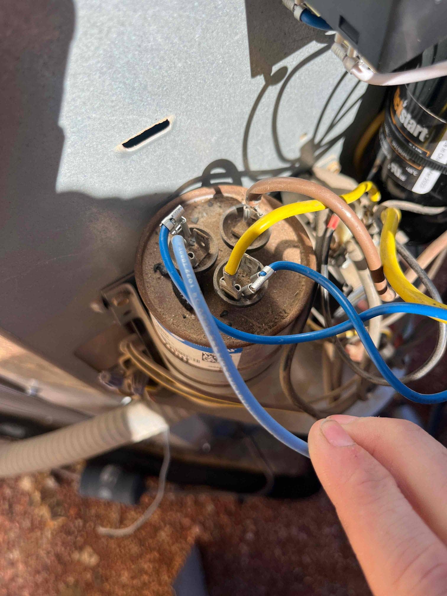 Old dual-run capacitor with attached blue, yellow, and brown wires, showing dusty top and intact quick-connect terminals.