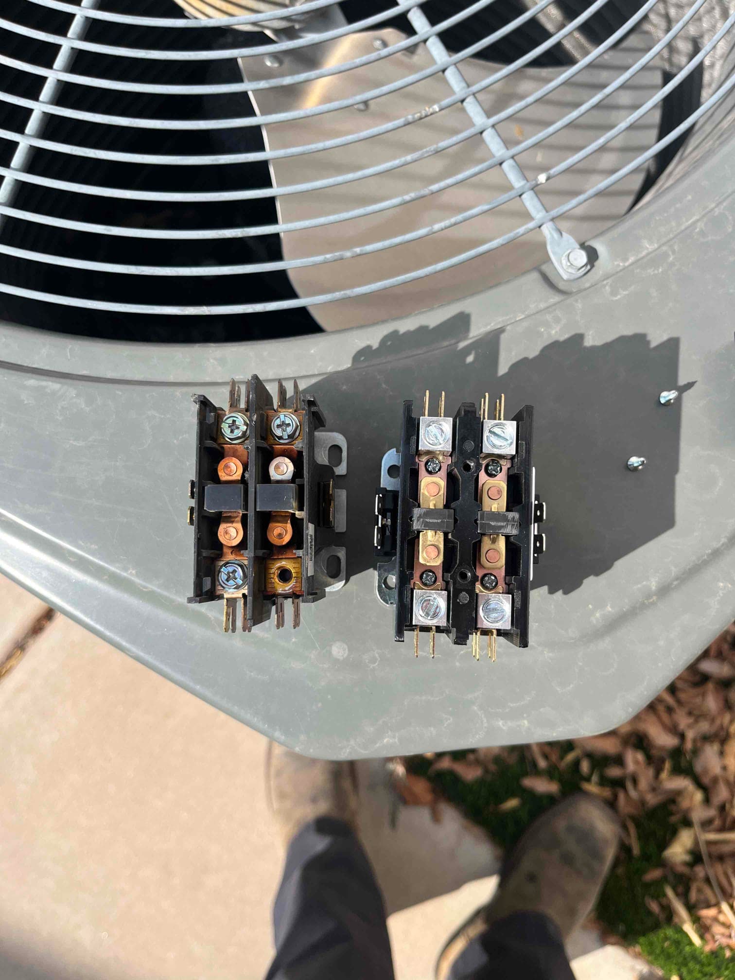 Old and new two-pole contactors placed on the condenser top, showing terminal screws and coil connections for replacement.