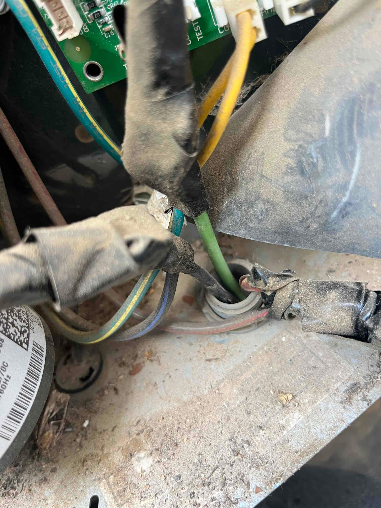 Outdoor condenser control compartment showing dust-covered wiring harness and insulated wire connections passing through the cabinet grommet.