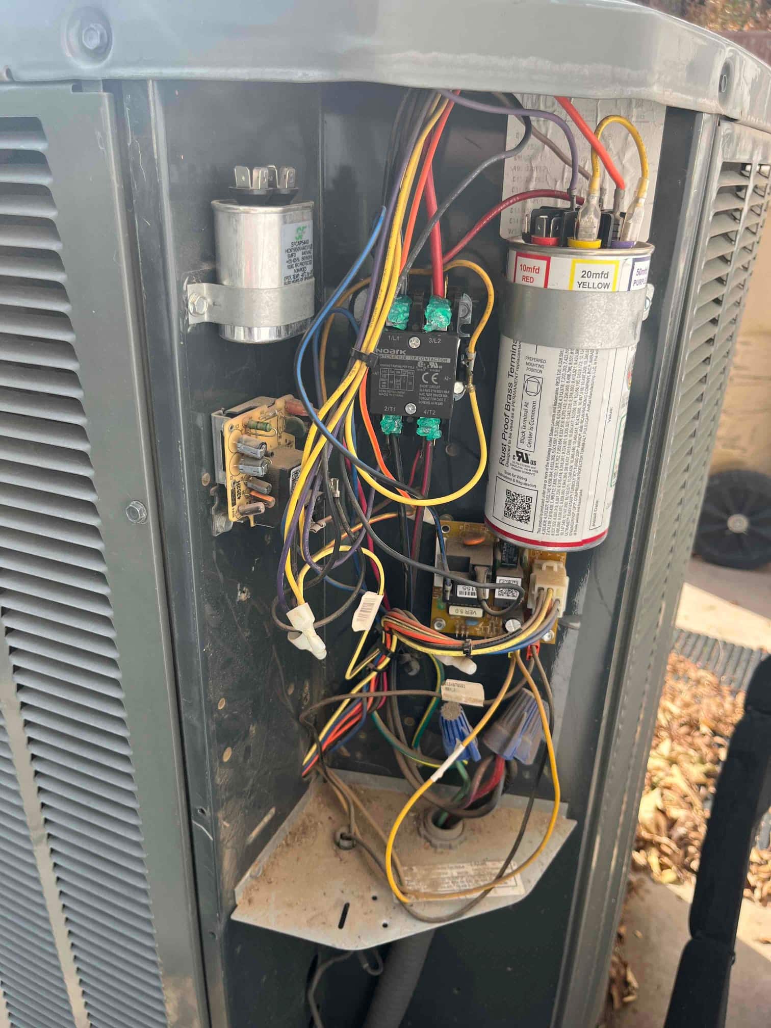 Outdoor condenser control compartment open, showing new contactor and ECM blower motor capacitor with connected wiring and terminals.