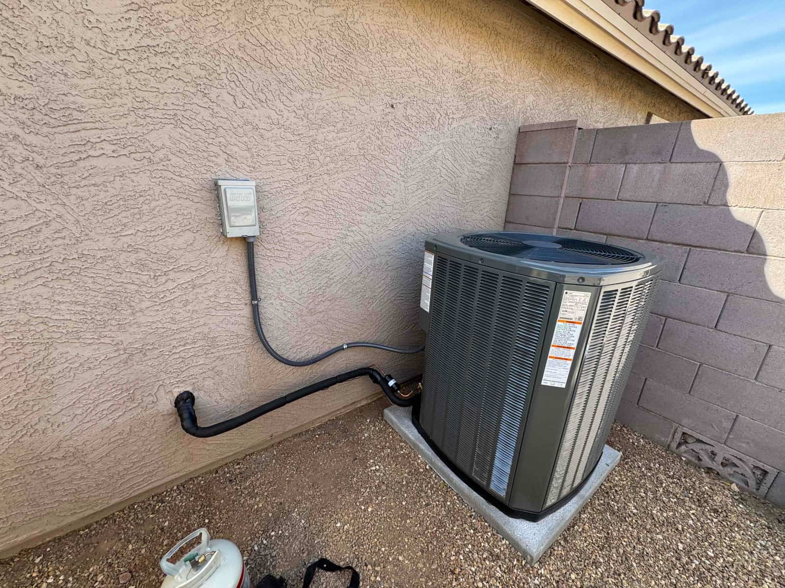 Outdoor condenser installed on a level pad with insulated line set and weatherproof disconnect mounted on the wall.