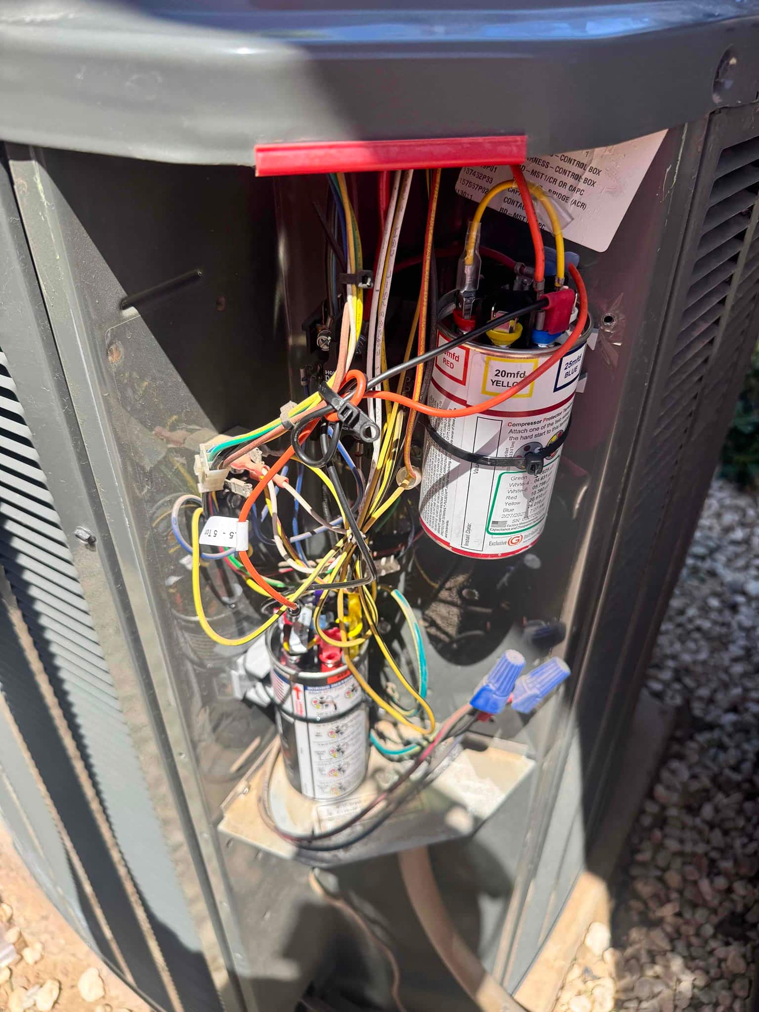 Outdoor condenser service panel open, showing newly installed dual-run capacitor and start assist with connected wiring and protective disconnect above.