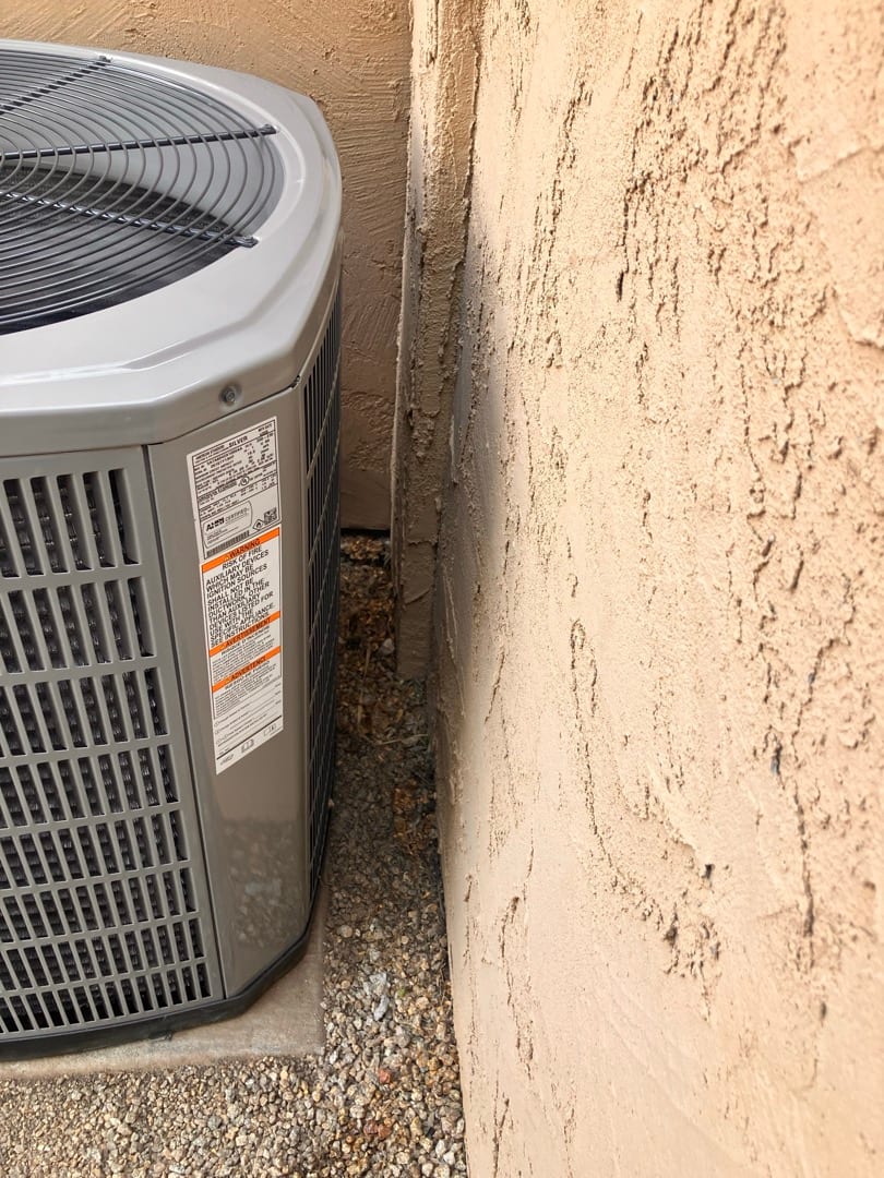Outdoor condenser set on a level pad beside a stucco wall, with proper side clearance and grille top visible.