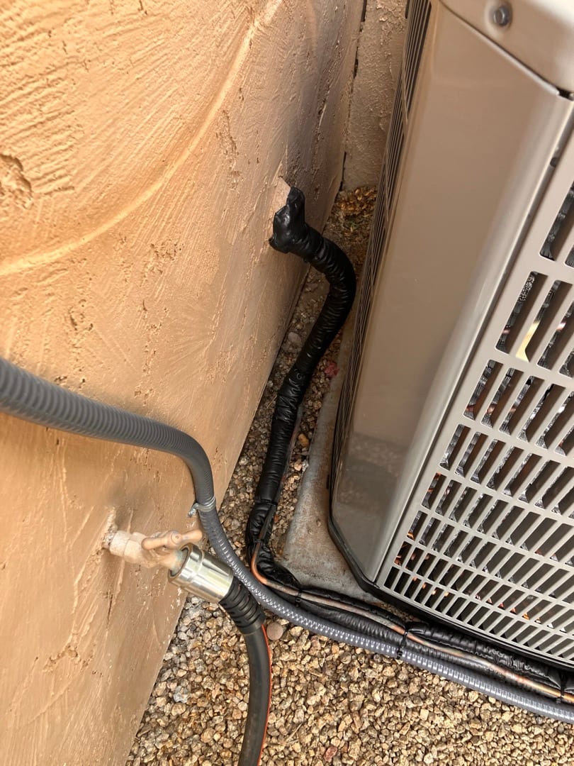 Outdoor condenser set on a pad with insulated refrigerant lines and electrical whip neatly routed to the wall penetration.