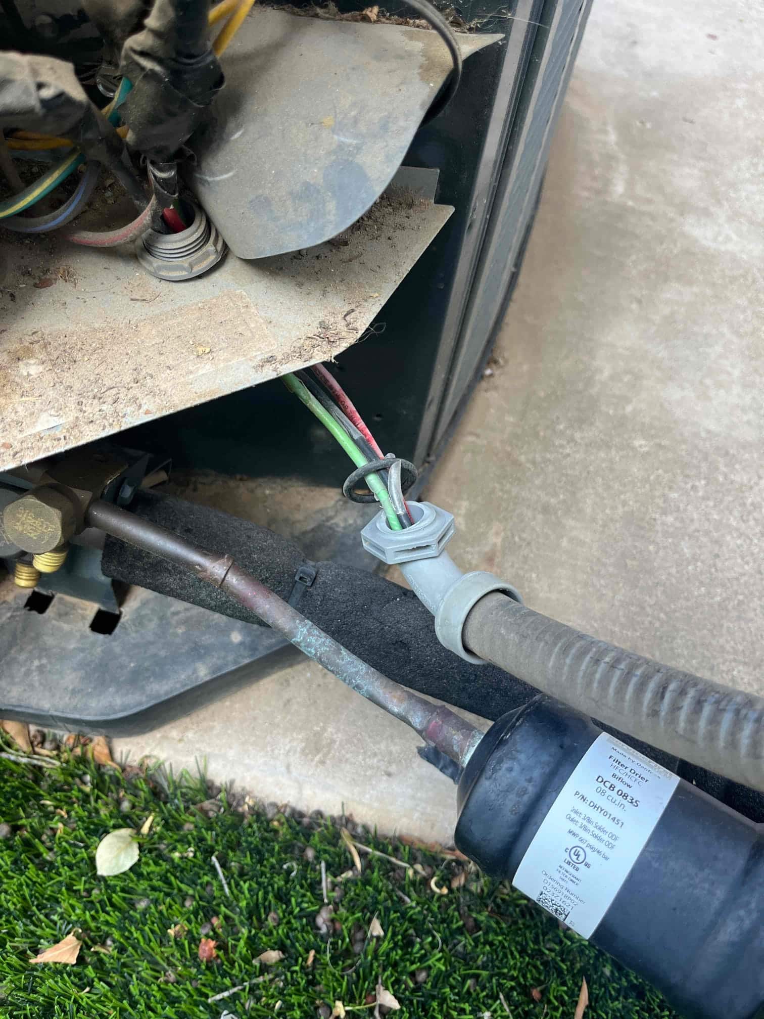 Outdoor condenser whip connection and wiring at the service panel, with flexible conduit and refrigerant line near the unit base.