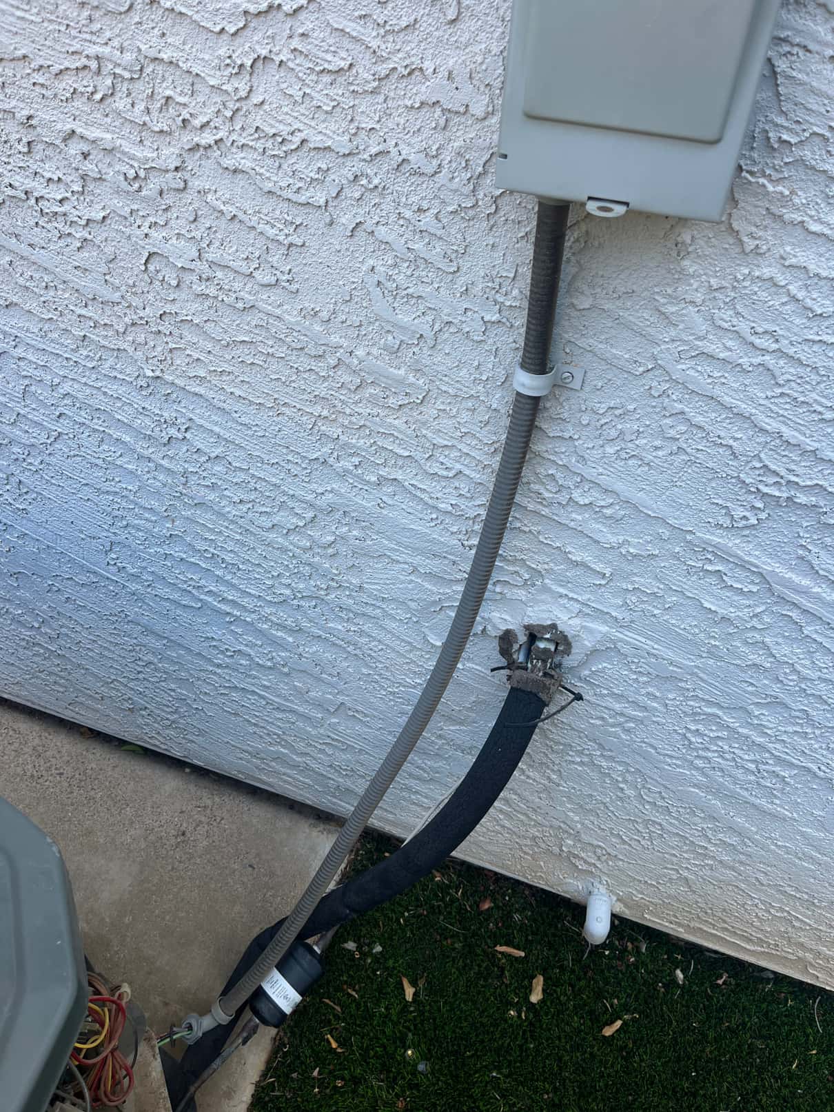 Outdoor condenser whip and electrical disconnect conduit at the wall, with insulated refrigerant line set and service access visible.
