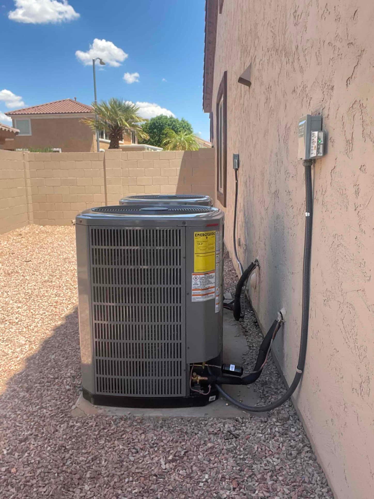 Two outdoor condensers set on level pads with insulated refrigerant lines and weatherproof disconnects mounted on the exterior wall.
