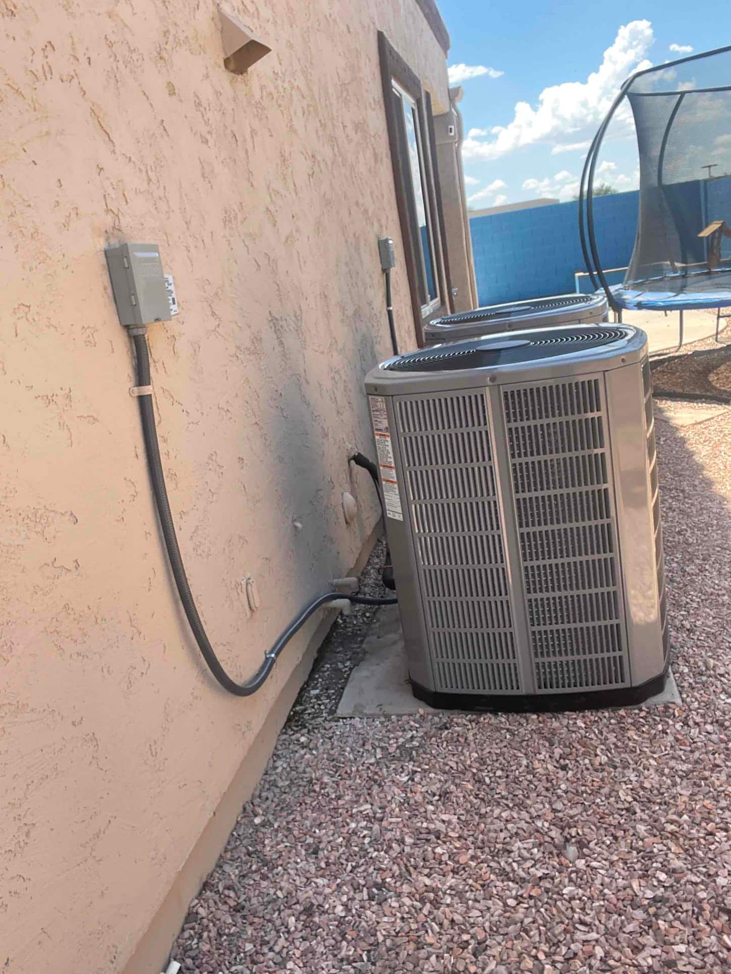 Two outdoor condensers set on level pads with secured electrical disconnects and insulated line sets along the exterior wall.
