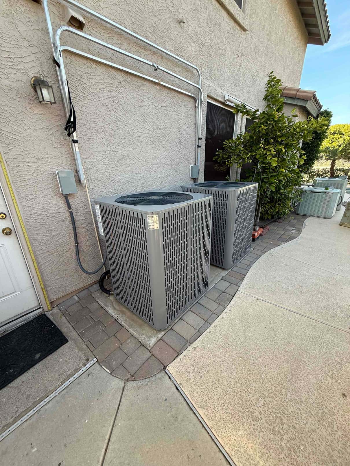 Two outdoor condensers set on level paver pads with sealed line set penetrations and exterior disconnect boxes mounted nearby.