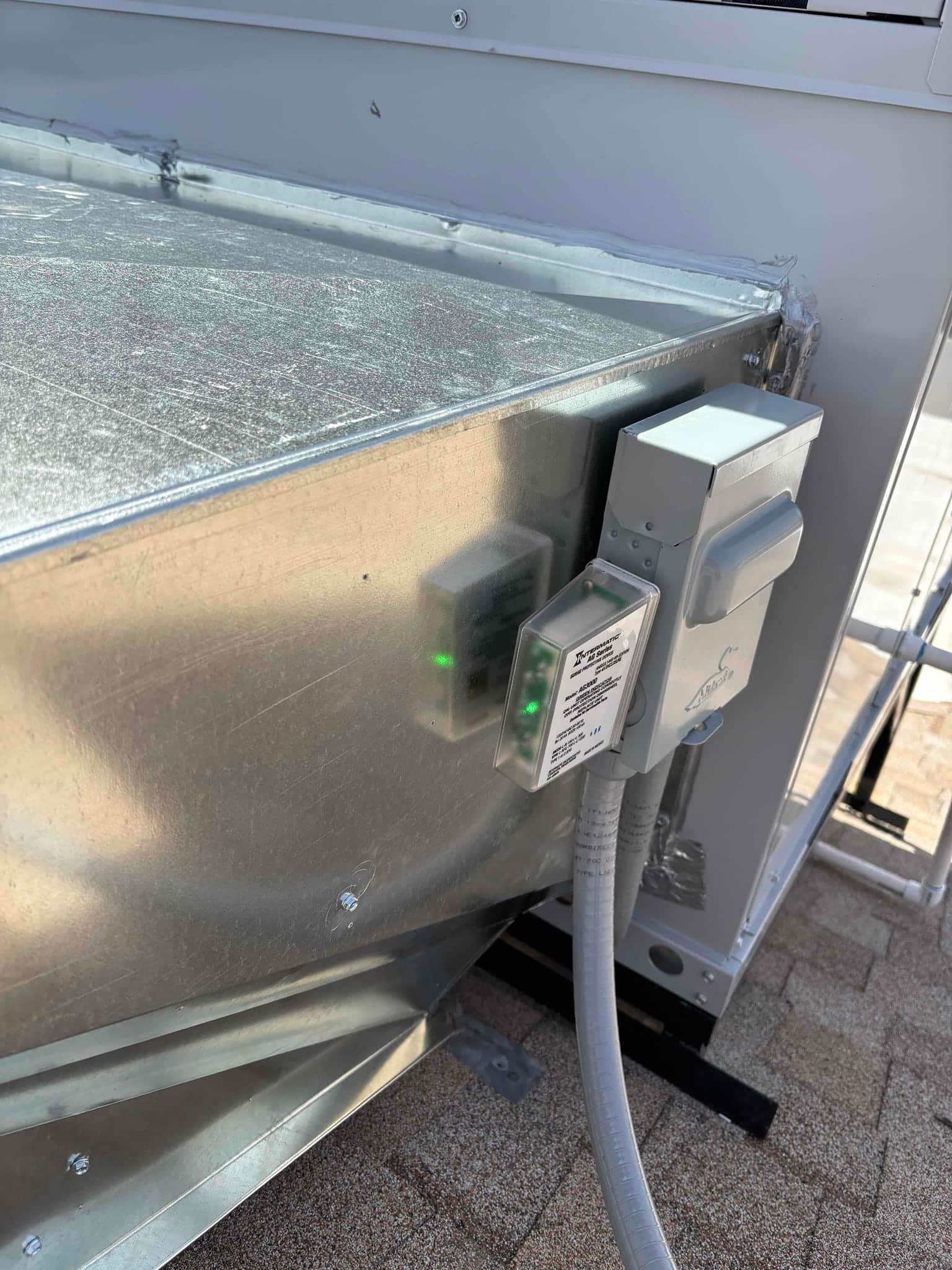 Outdoor disconnect and surge protection mounted beside the packaged unit with sealed conduit and metal curb flashing visible.