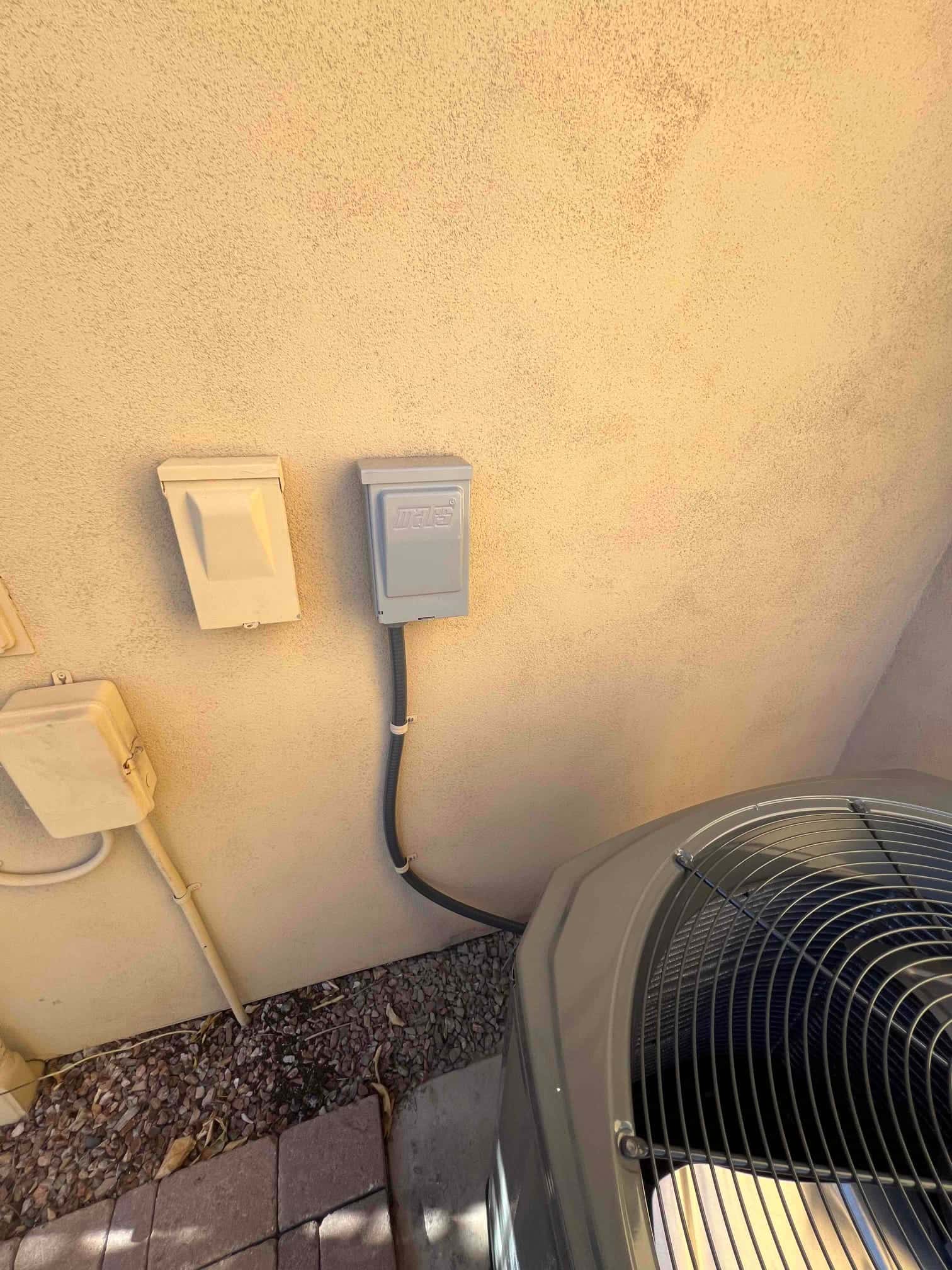 Outdoor disconnect and whip neatly installed beside the new heat pump condenser on a level pad with secured conduit.