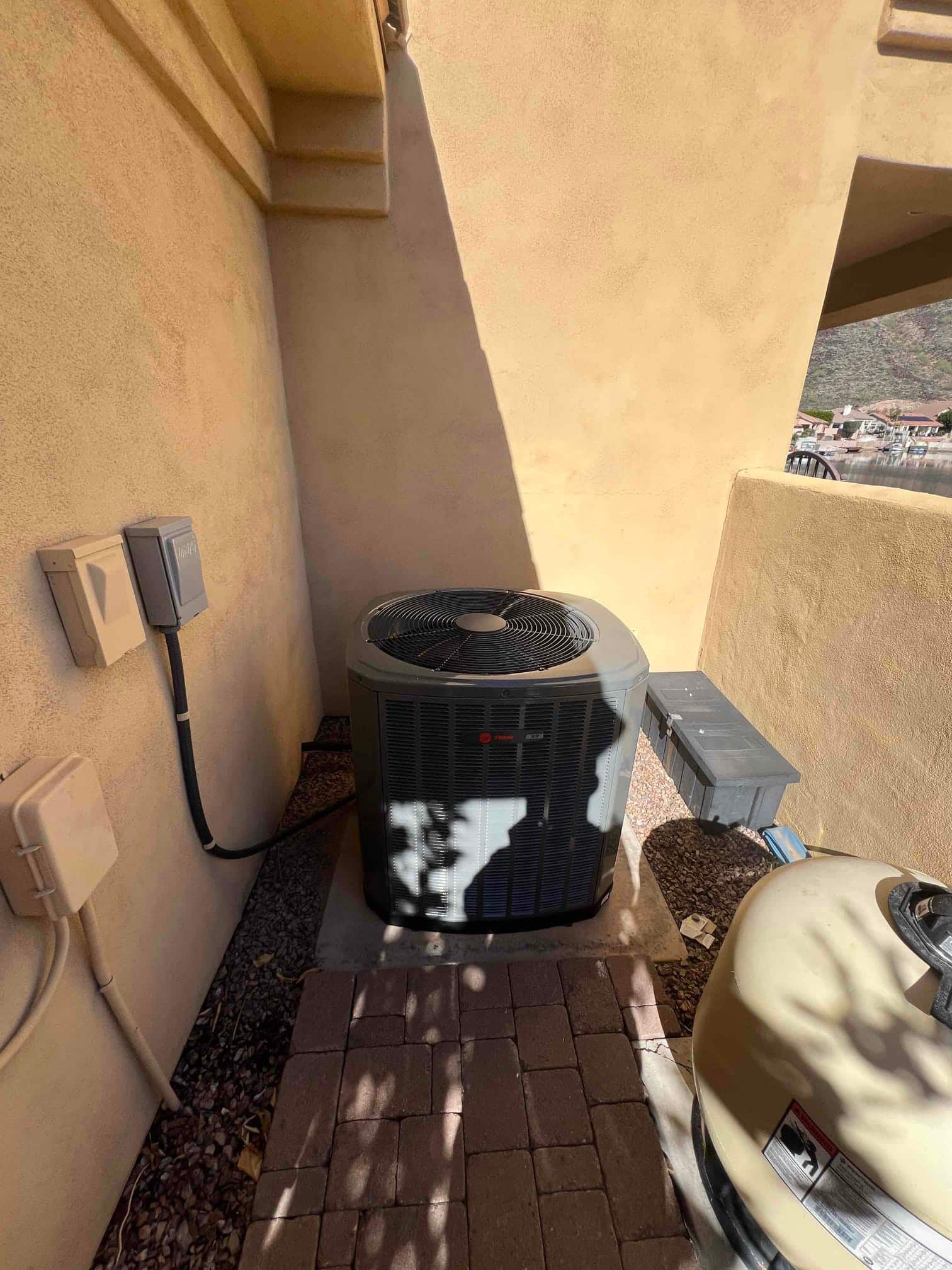 Outdoor heat pump condenser set on a level pad with electrical disconnects mounted on the wall and clear service access.