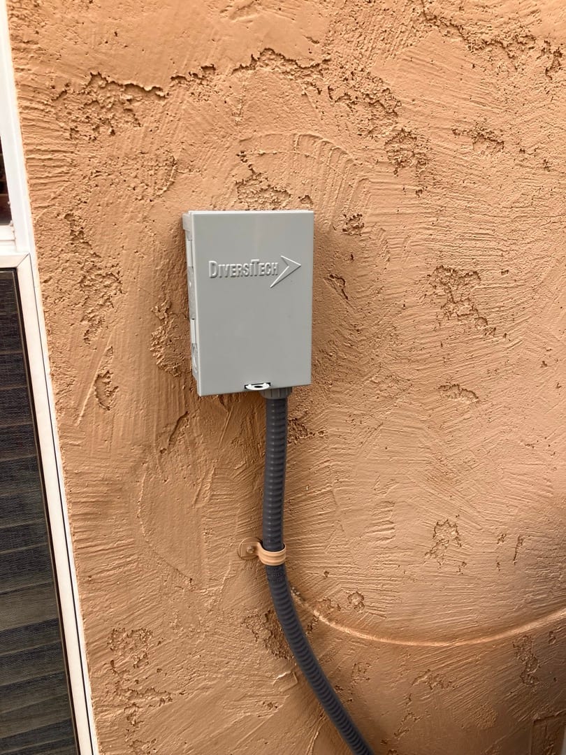 Outdoor HVAC disconnect box mounted on stucco wall with flexible conduit secured and routed to the condenser.