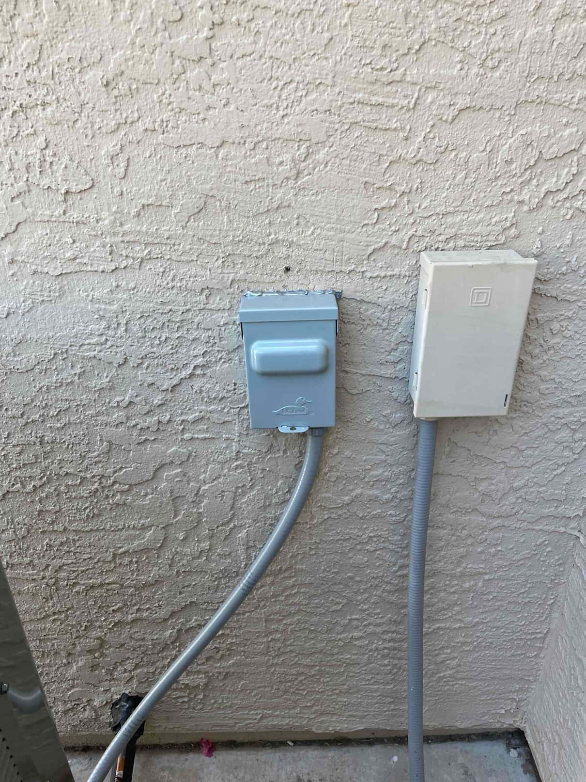 Outdoor HVAC disconnect and whip installed on exterior wall beside control box, with flexible conduit routed to the condenser.