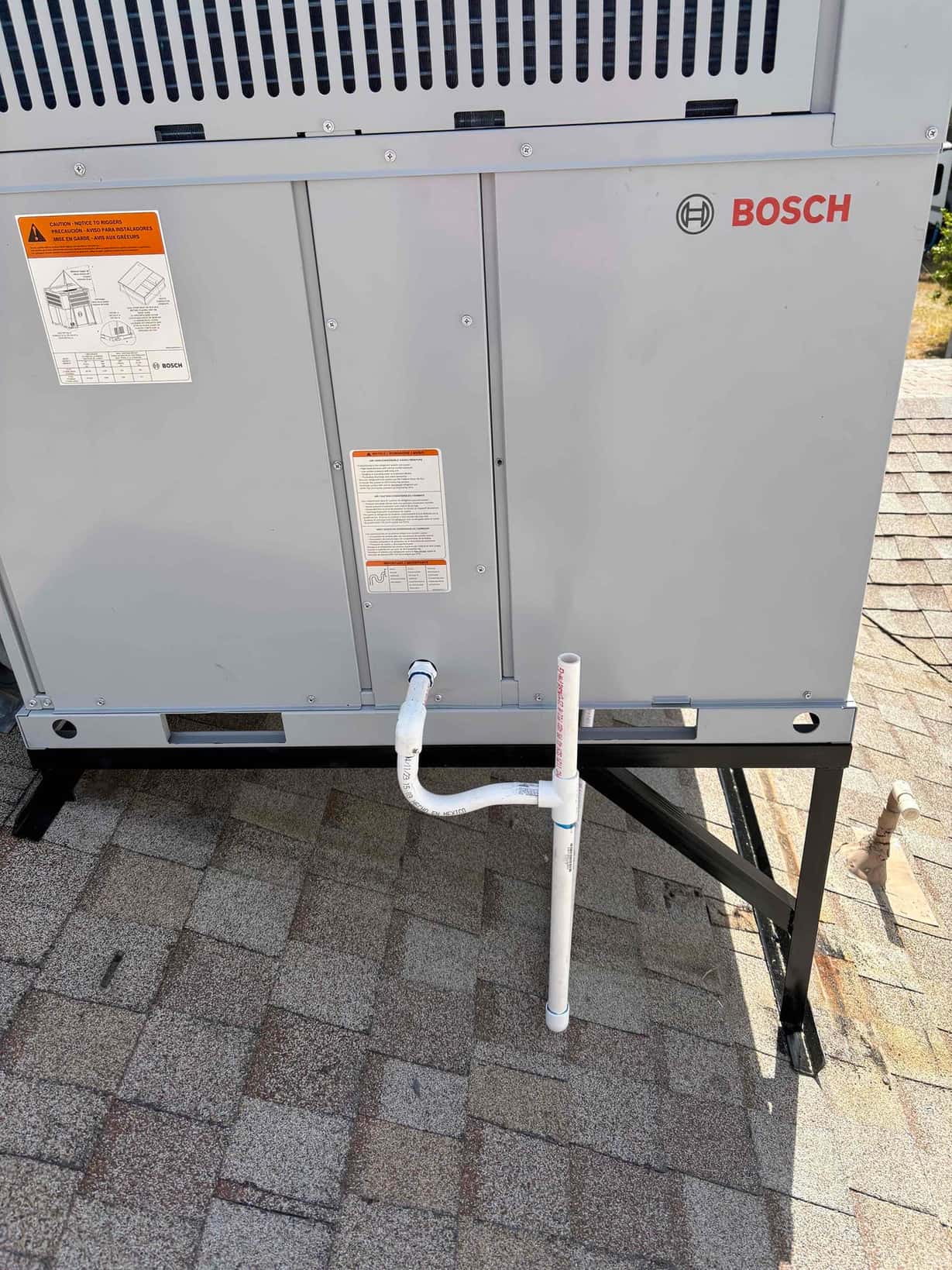 Packaged rooftop heat pump set on a steel stand with newly installed PVC condensate drain assembly exiting the cabinet.