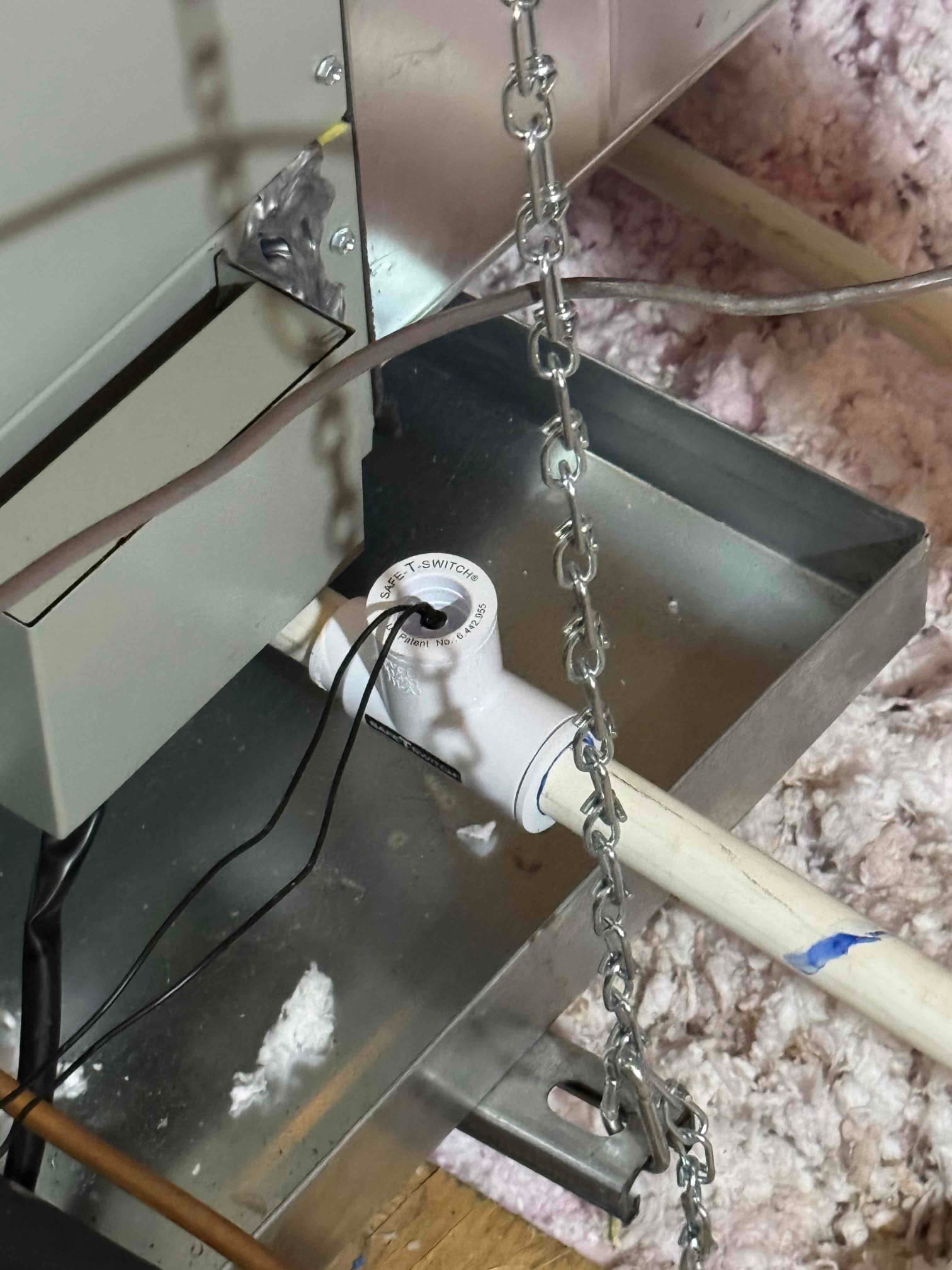 Primary drain line with in-line float safety switch installed over a metal secondary drain pan beneath a suspended air handler.