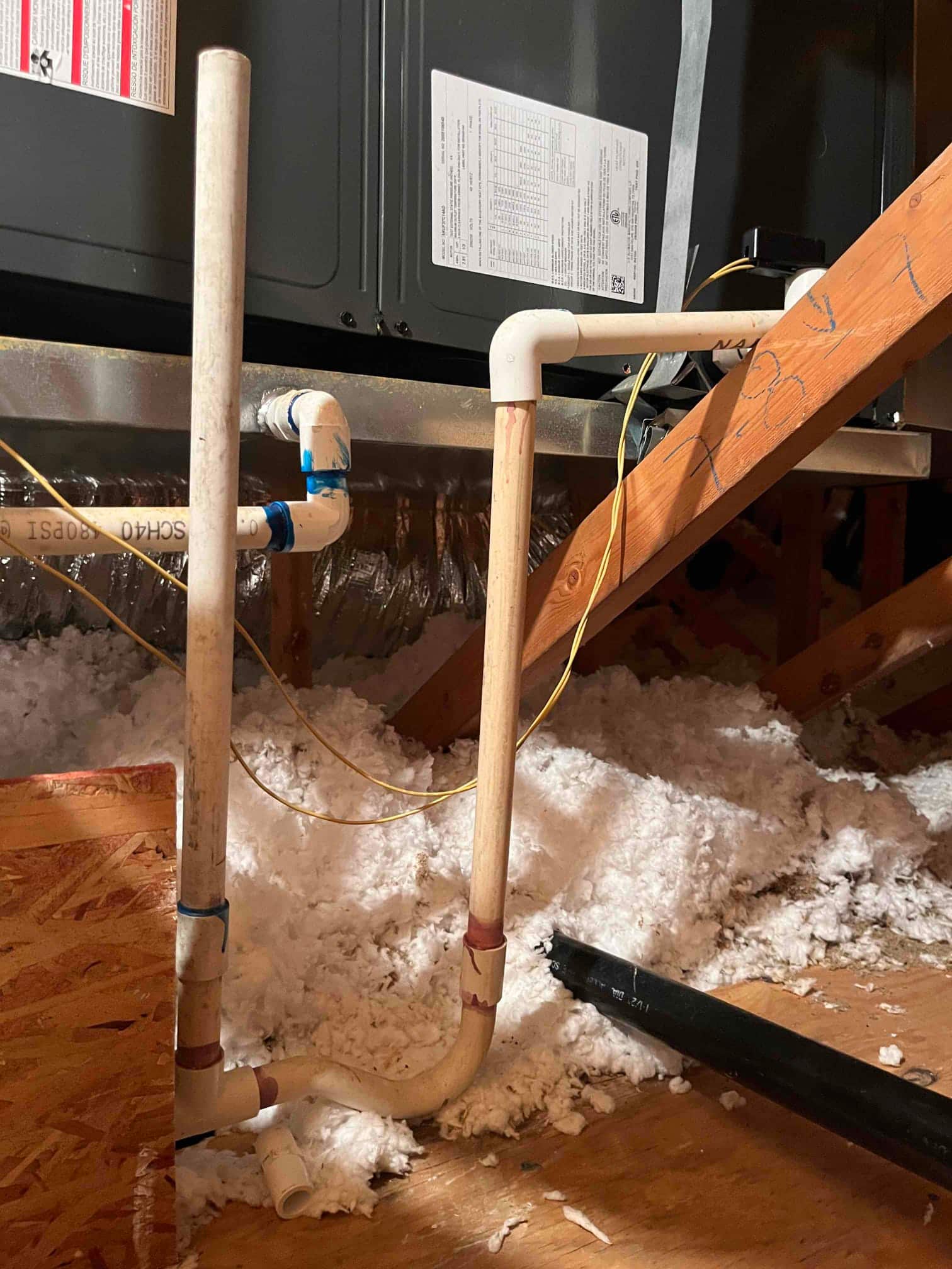 PVC condensate drain line with cleanout and trap connected to an air handler in the attic insulation.