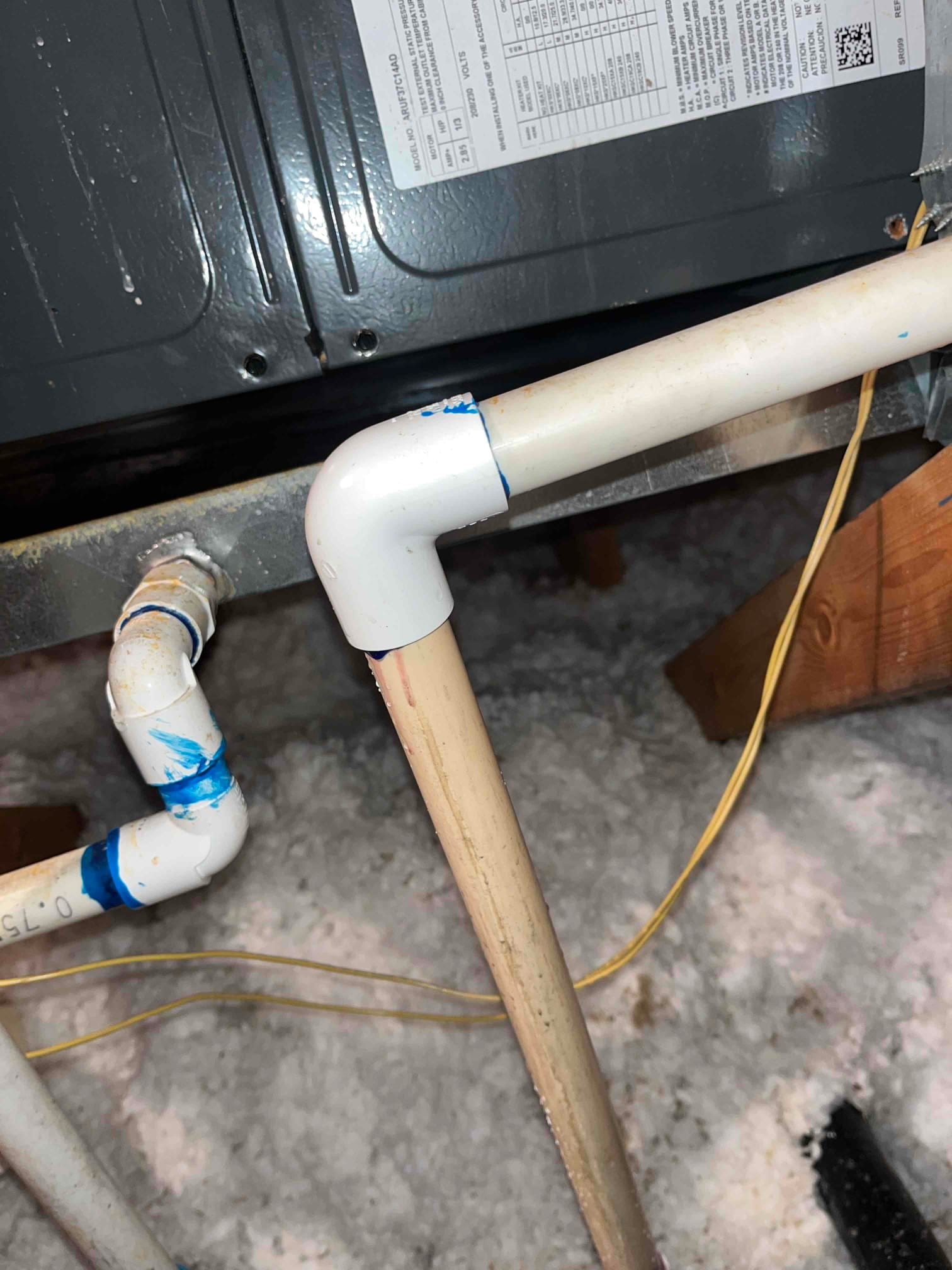 PVC condensate drain line with multiple elbow fittings and blue solvent marks near the indoor air handler in an attic.