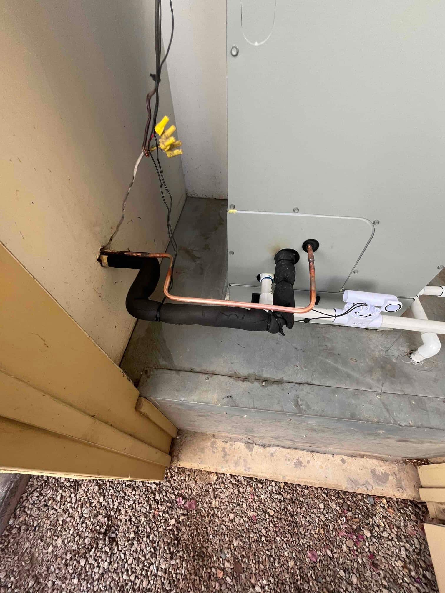 Refrigerant line set with insulation and condensate drain connected to a newly installed indoor unit on a concrete pad.