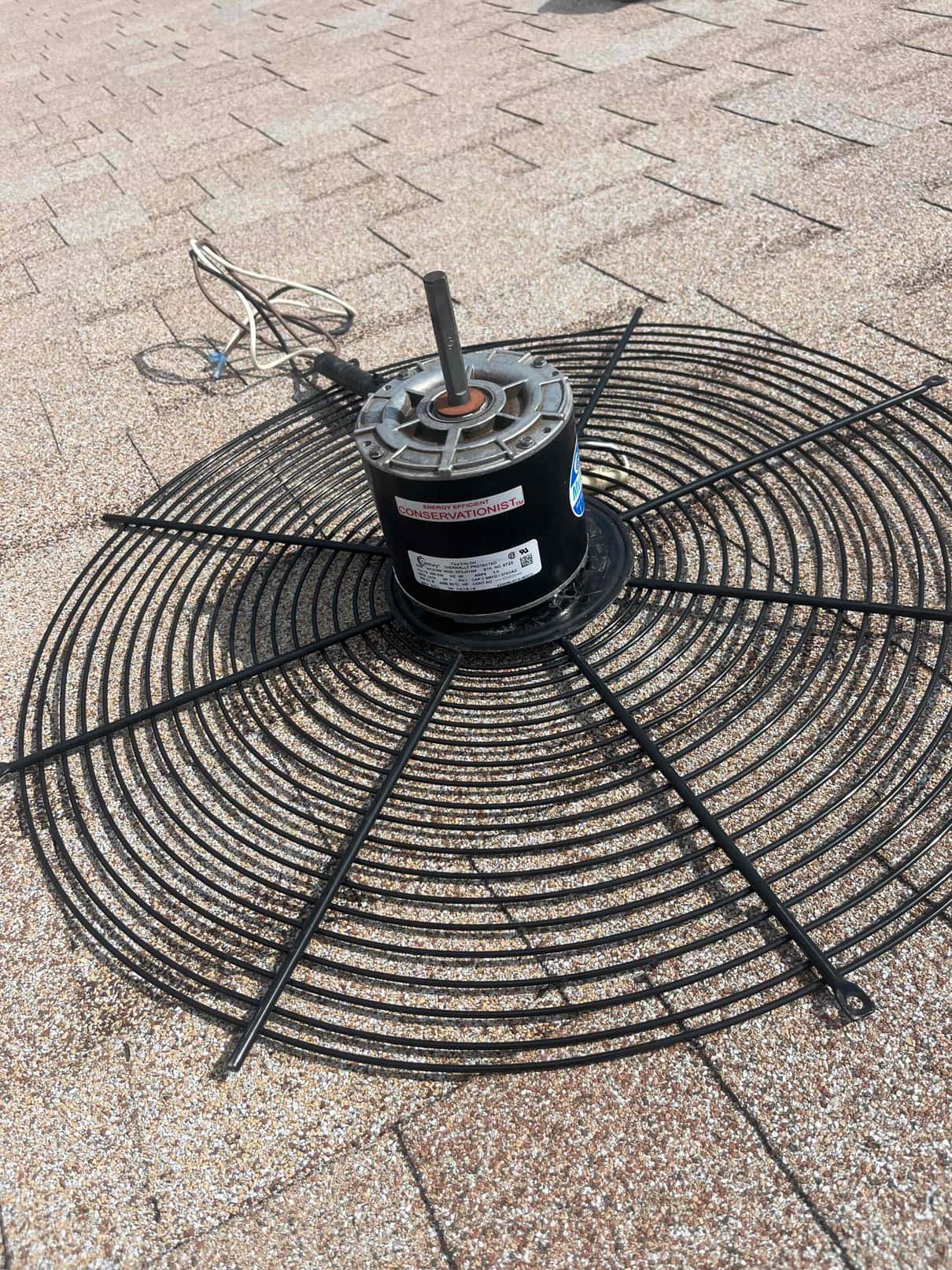 Removed condenser fan motor placed on the fan guard, showing shaft and housing ready for replacement during repair.
