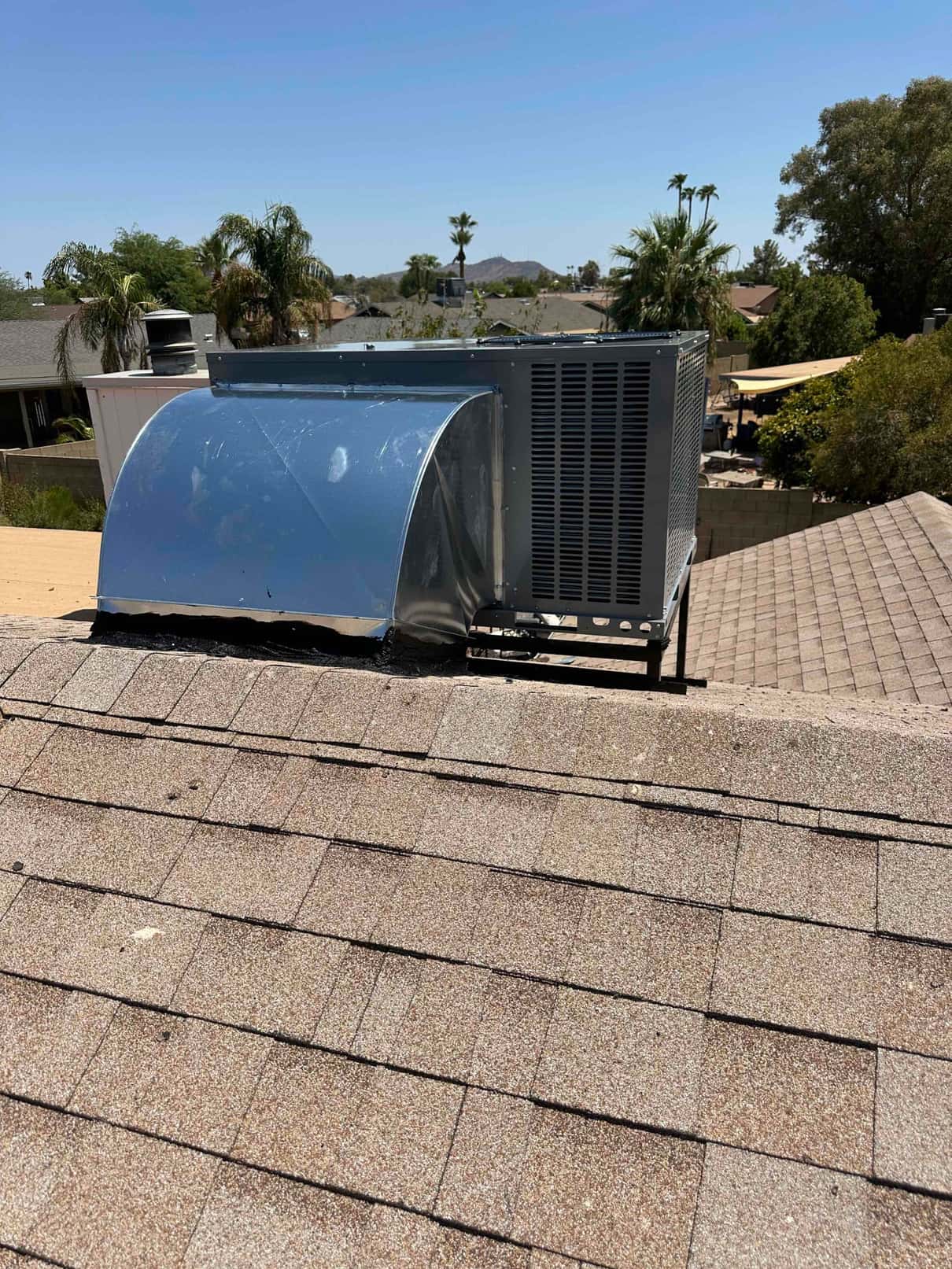 Rooftop package HVAC unit installed on a curb with sheet metal transition and secured mounting on shingle roof.