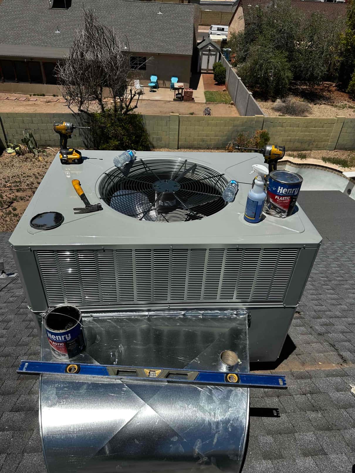 Rooftop package HVAC unit set in place with sheet metal transition, sealant, and tools during installation work.