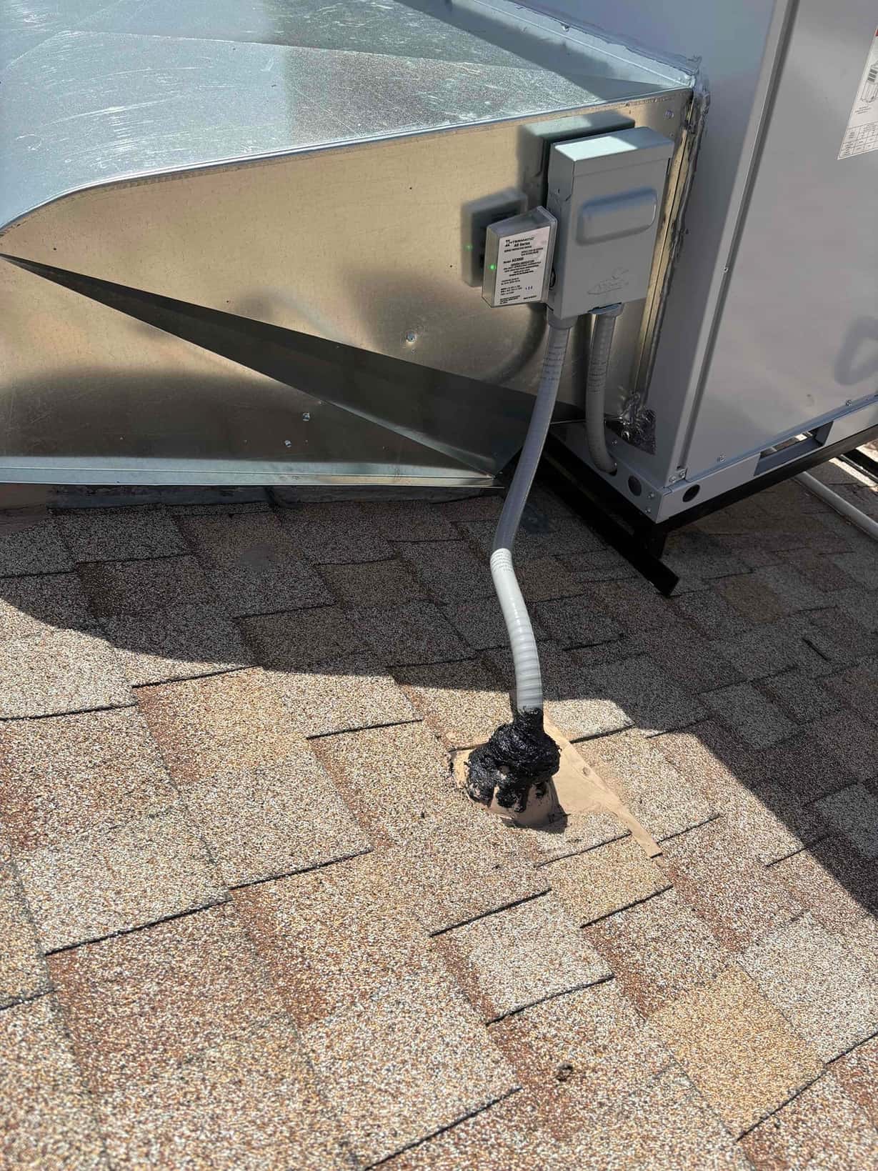 Rooftop packaged unit with weatherproof disconnect and flexible conduit sealed at the roof penetration next to the curb.