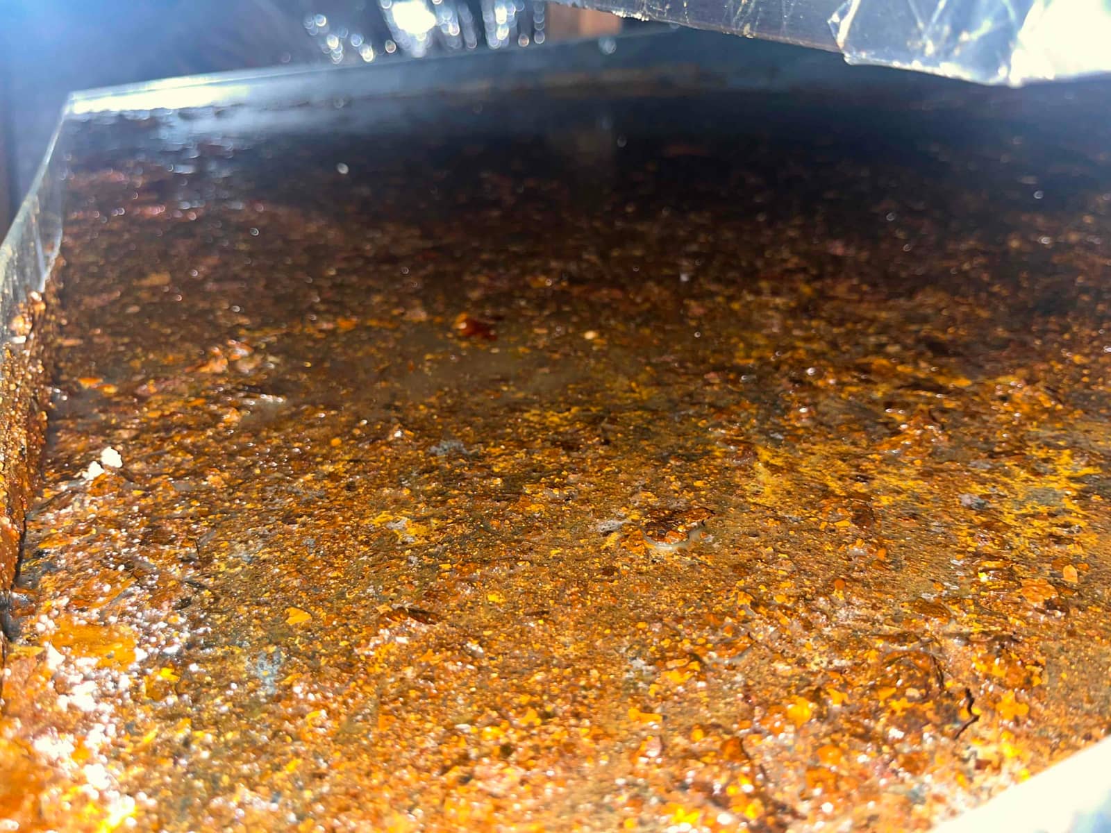 Rust-covered condensate drain pan inside an air handler, showing heavy corrosion and standing water contamination under the evaporator area.