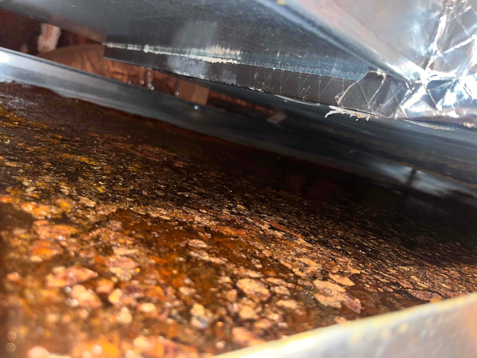 Standing water and rust inside an air handler drain pan, showing evidence of condensate buildup and corrosion around the drain area.
