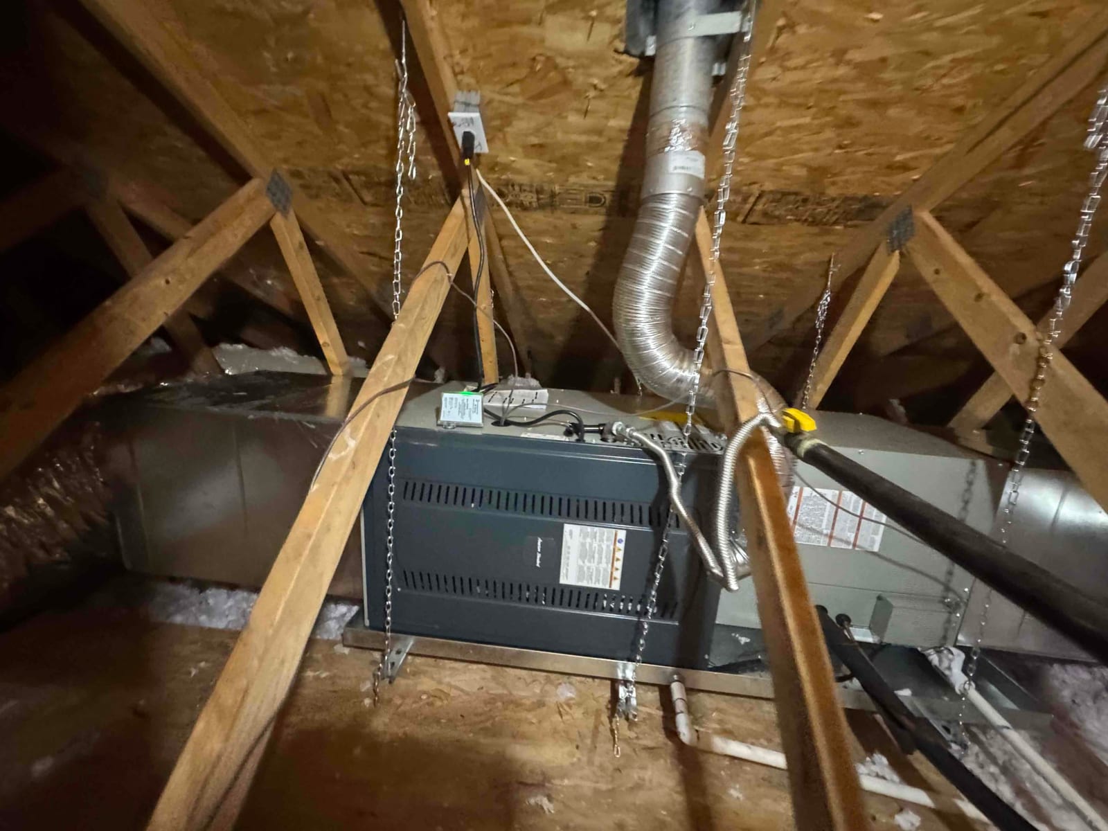 Suspended attic air handler and ductwork installed with hanging chains, insulated flex duct, drain piping, and electrical whip connected.