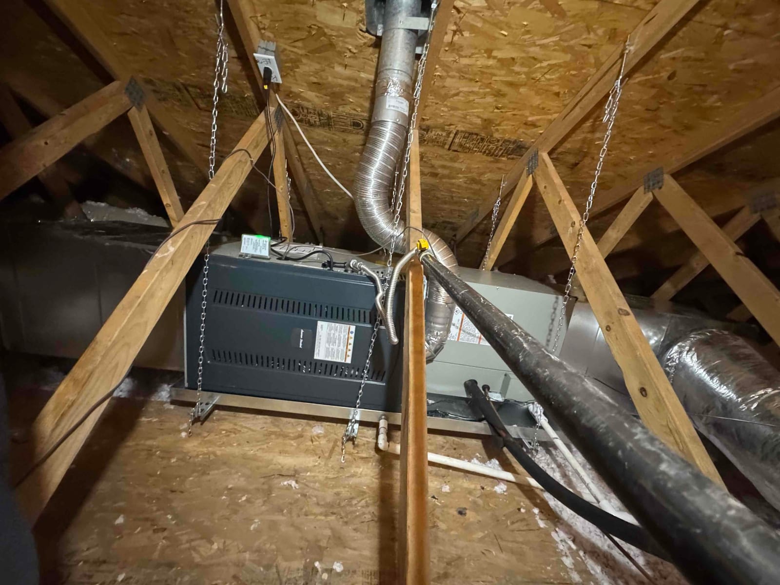 Suspended attic air handler installation with insulated ducts, drain lines, and electrical whip secured between roof trusses.