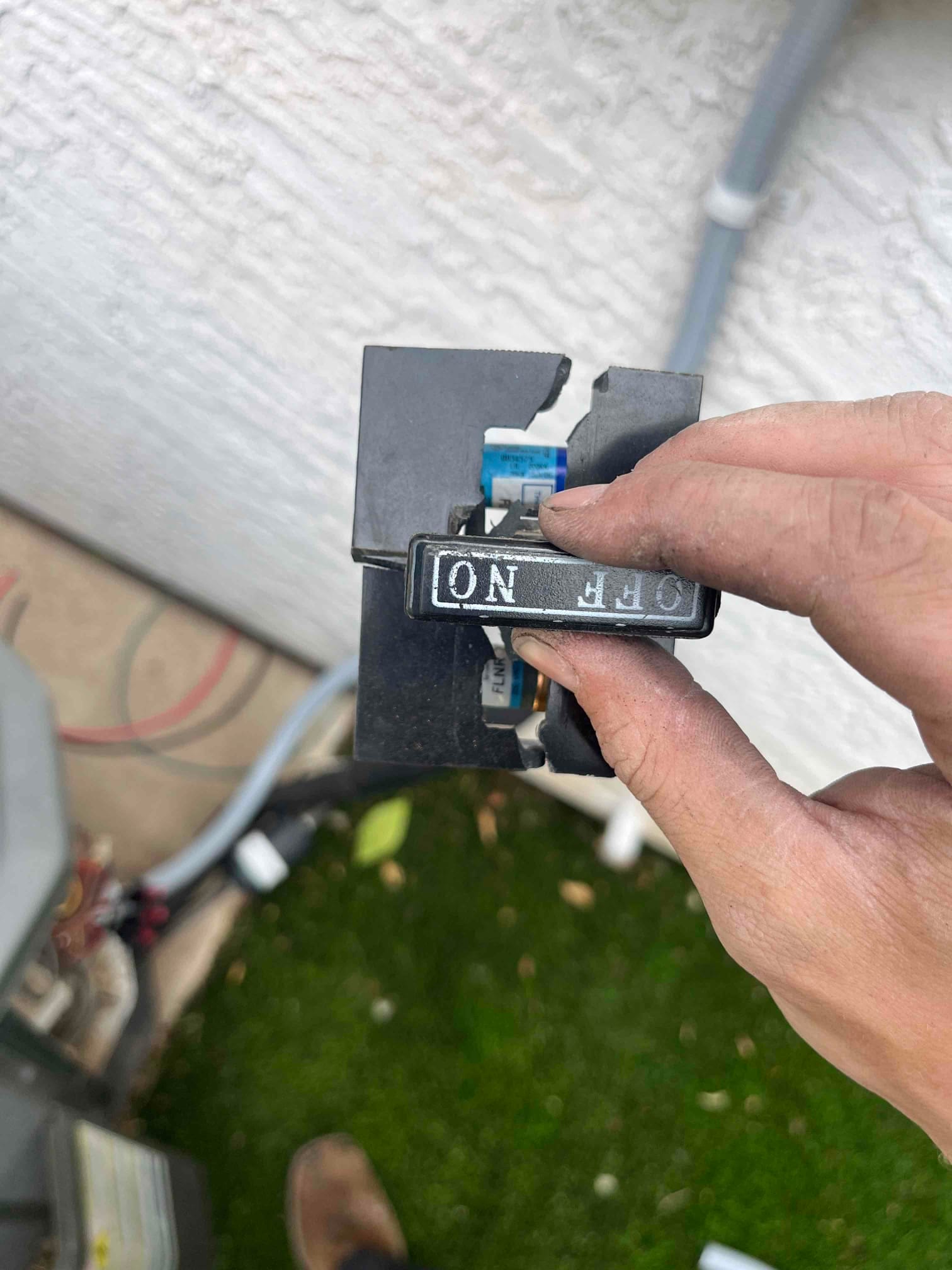 Technician holds a damaged outdoor disconnect switch with a broken handle and exposed fuse block near the condenser.