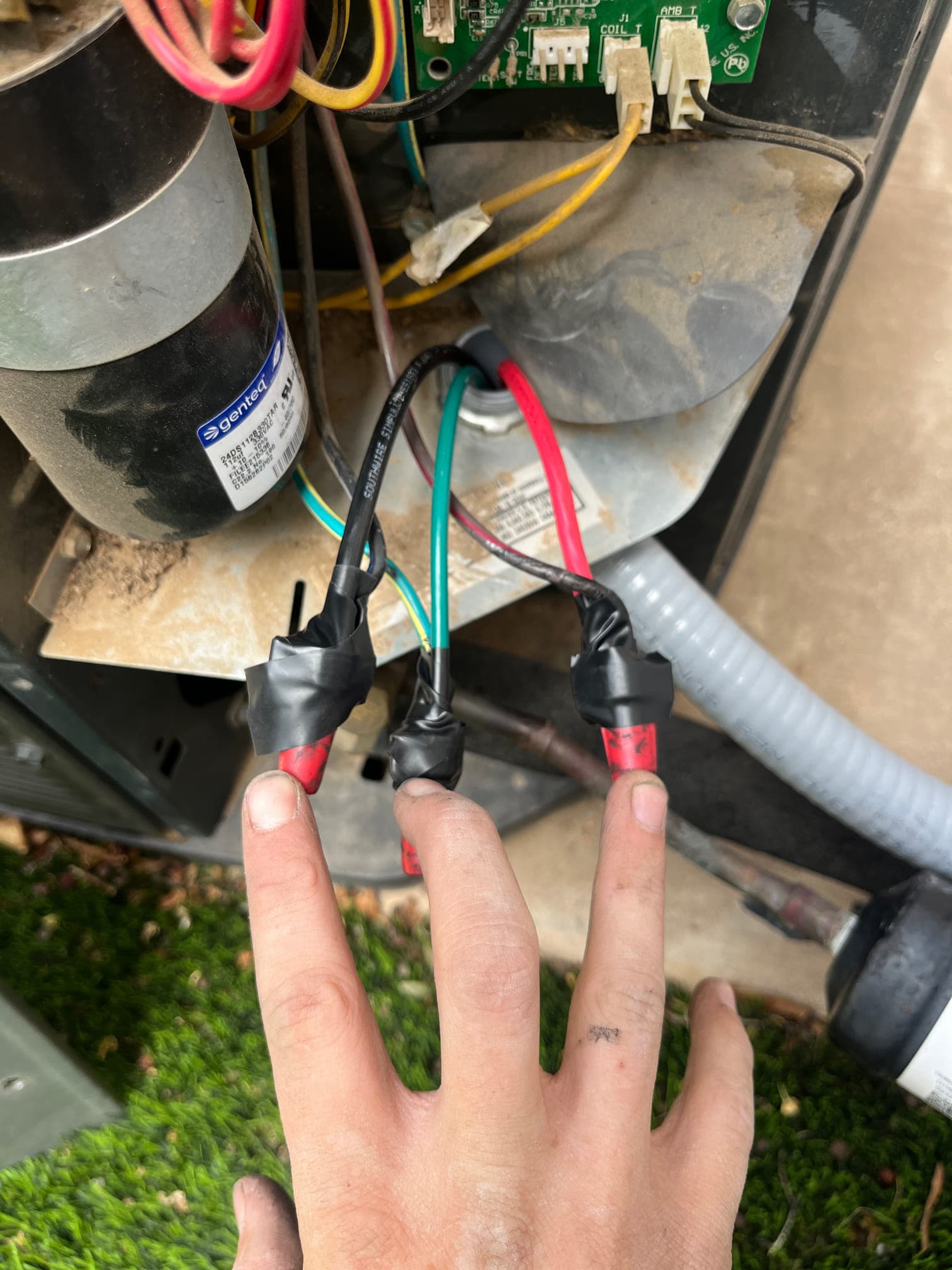 Technician shows three newly spliced condenser whip conductors with insulated connectors and electrical tape near the outdoor unit control compartment.