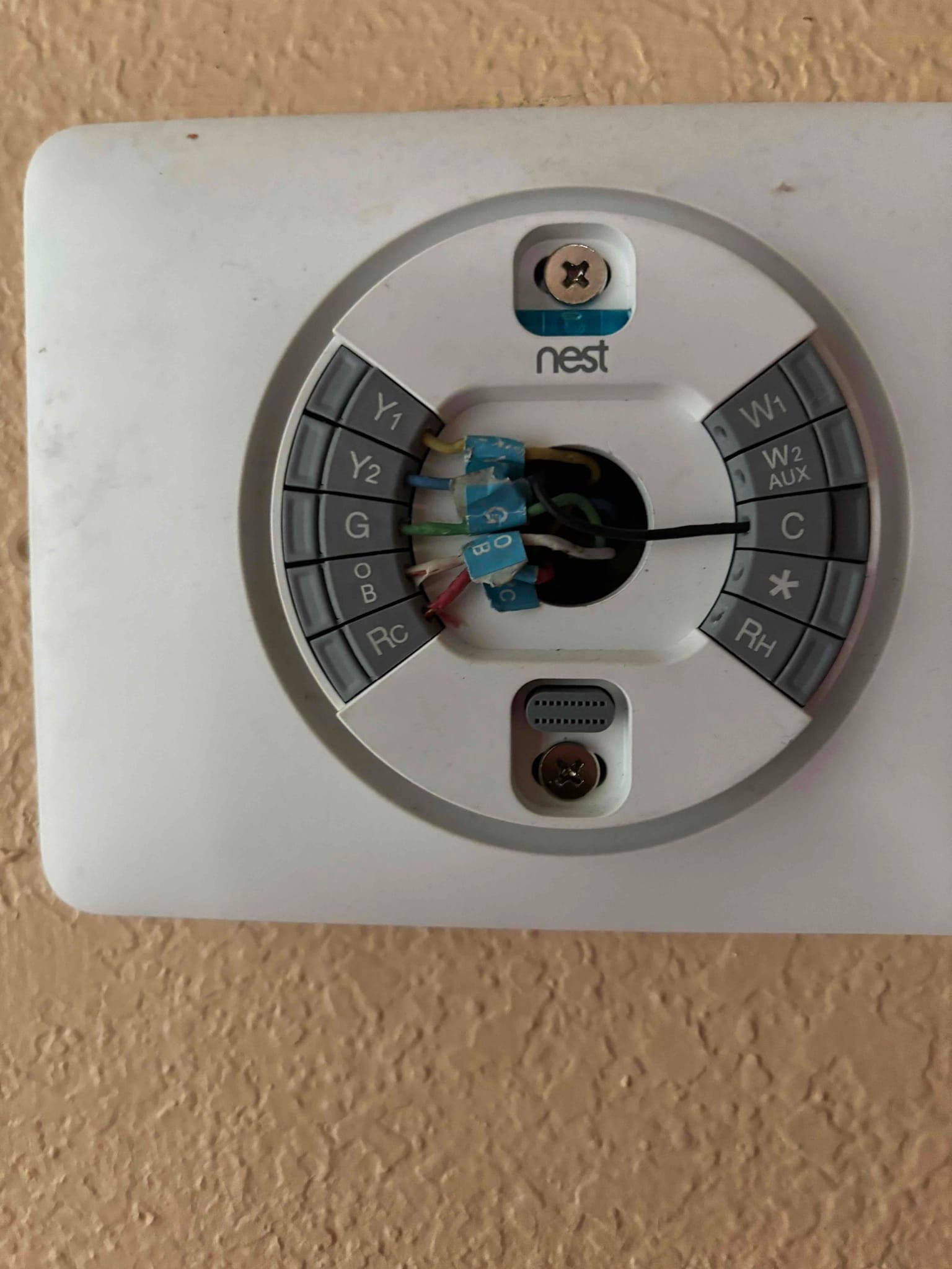 Thermostat base with control wires connected at labeled terminals, mounted on an interior wall during system installation.