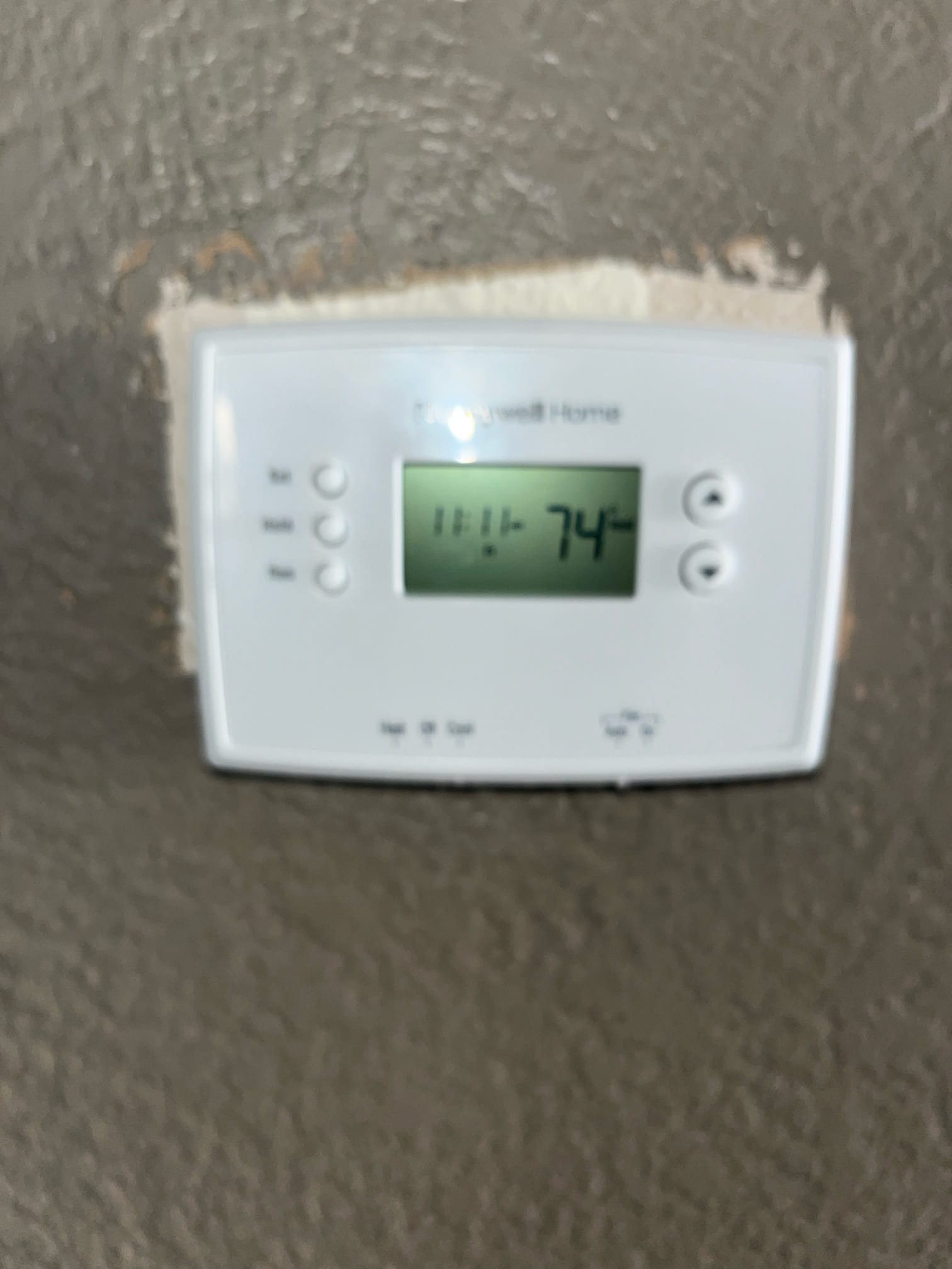 Wall-mounted digital thermostat displays 74 degrees with system on, showing time and control buttons for mode and fan.