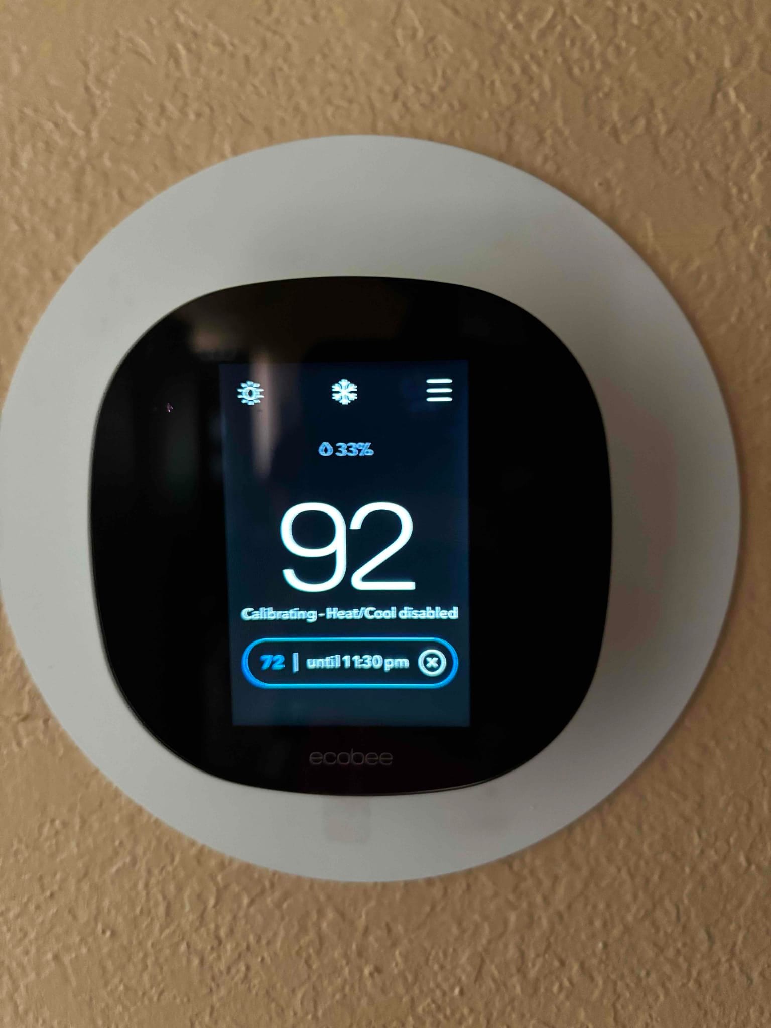 Wall-mounted smart thermostat displays 92 degrees and a message indicating calibration with heating and cooling temporarily disabled.