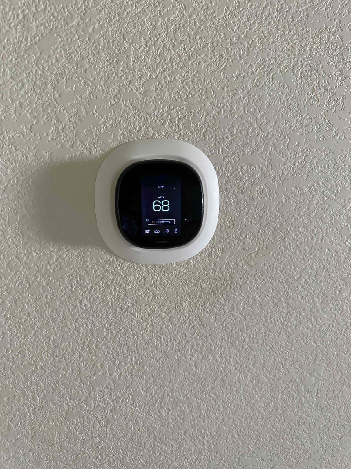 Wall-mounted smart thermostat installed on a finished wall, display showing 68 degrees with system mode off.